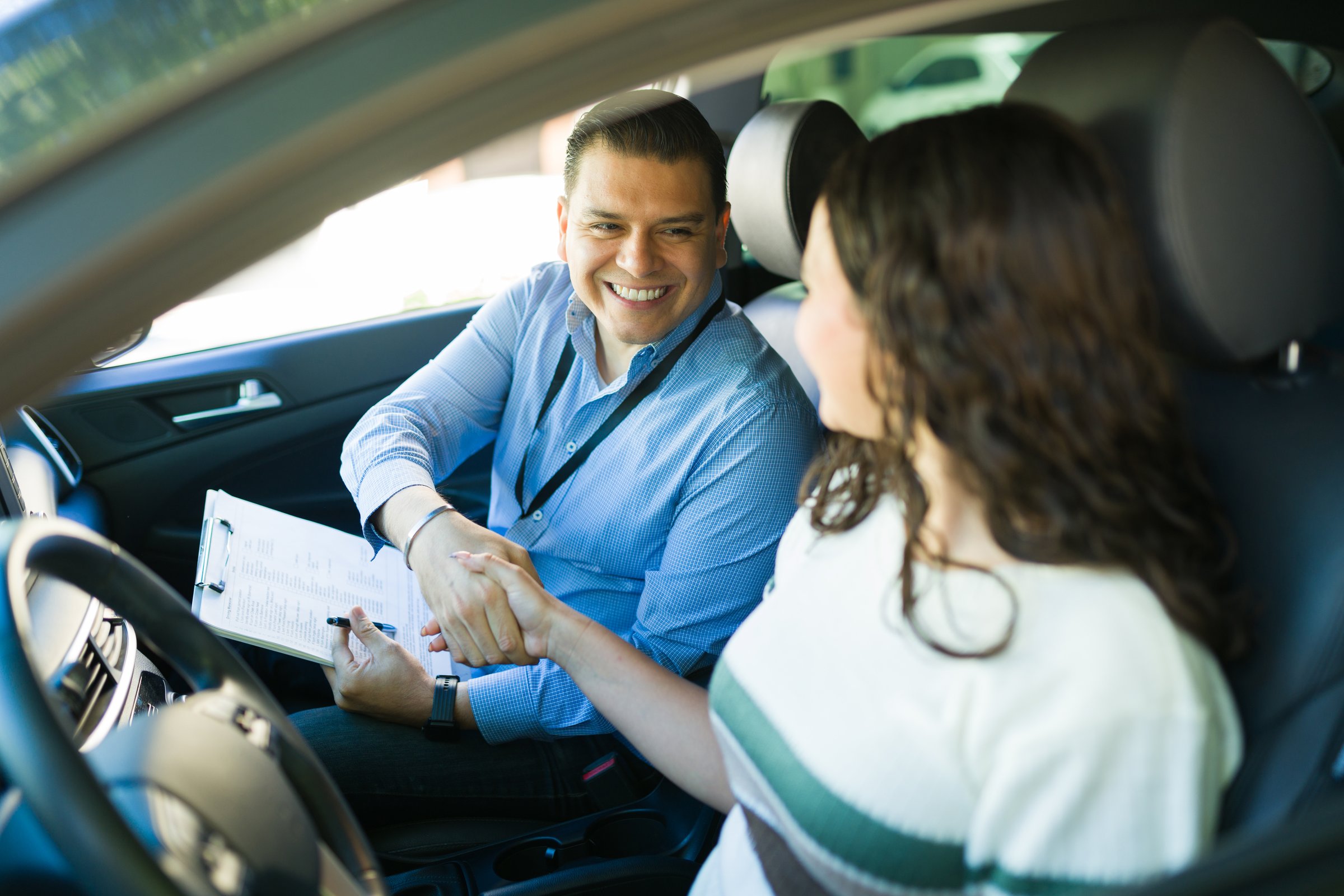 Joyful driving instructor congratulating his student after successfully passing the driving test in a car