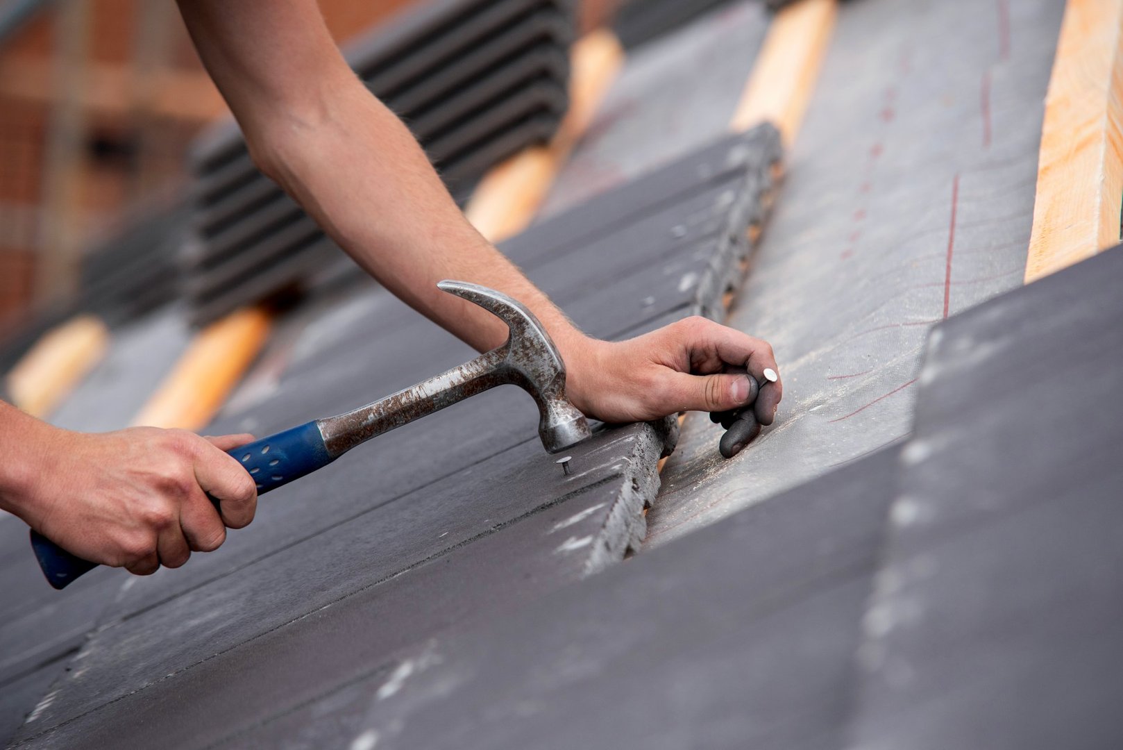 Close-up of skilled builder hands carefully placing roofing tiles on sloped surface of building and using hammer to ensure proper alignment