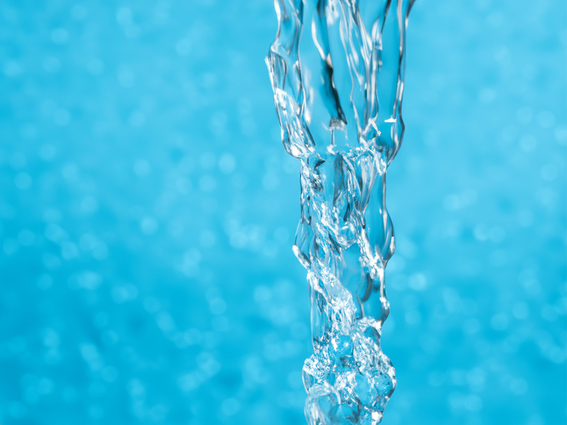 Close-up of clear water pouring against a blurred blue background, capturing the fluid motion and transparency.