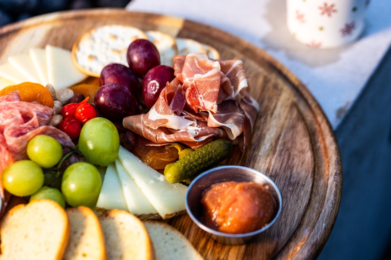 Gourmet charcuterie platter on rustic wood featuring prosciutto, salami, artisan cheeses, green olives, grapes, dried apricots, pickles and savory dipping sauce