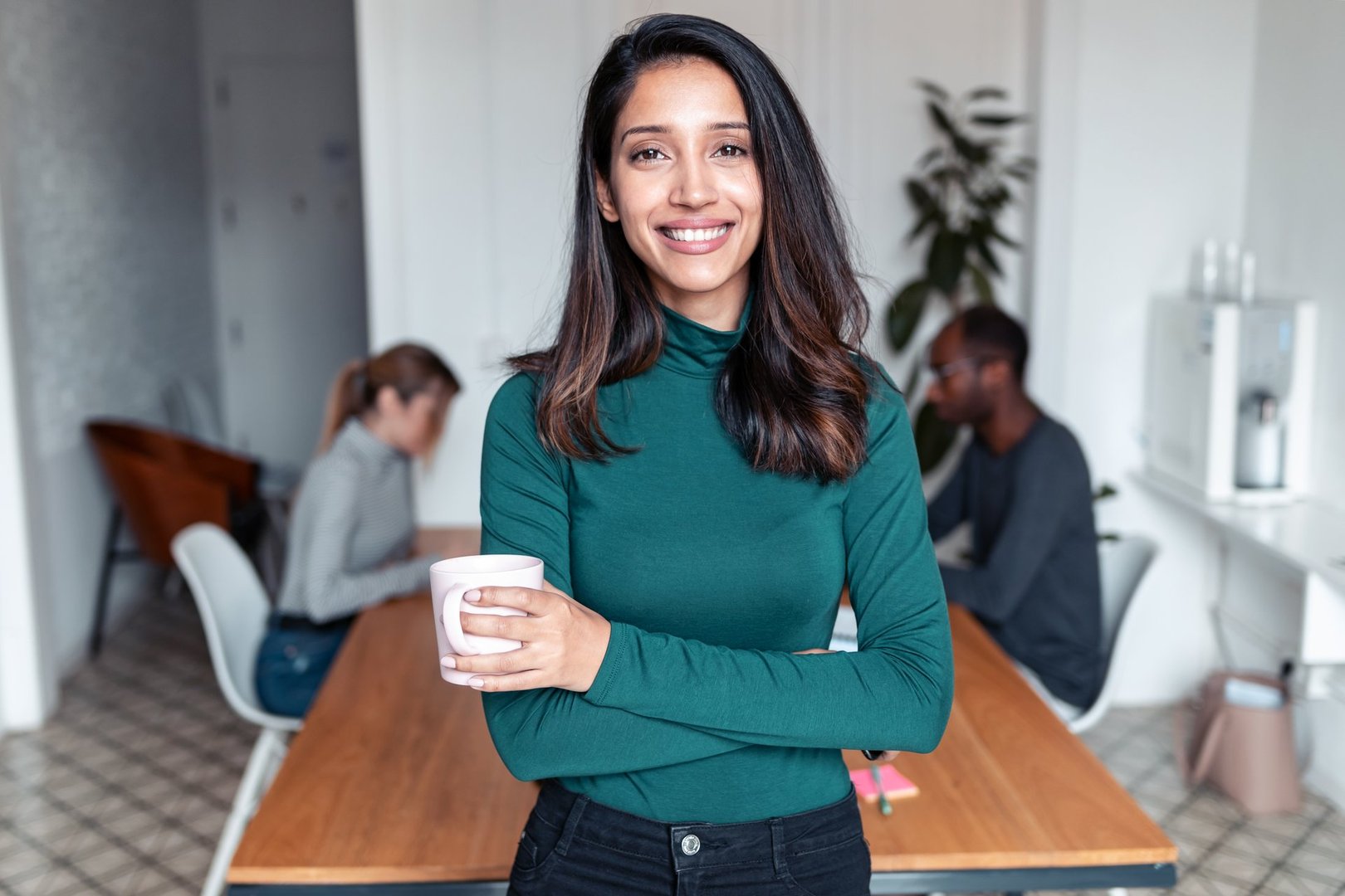 Shot of young indian business woman entrepreneur looking at camera in the office. In the background, her colleagues working.