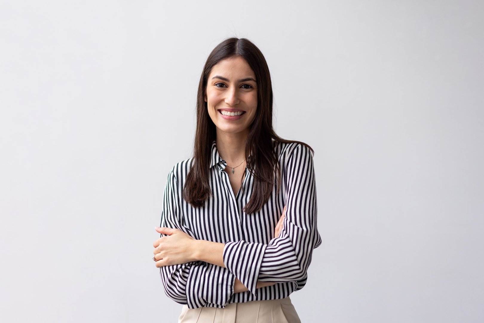 Portrait of a confident young businesswoman smiling with arms crossed, embodying professionalism and ambition against a clean white background