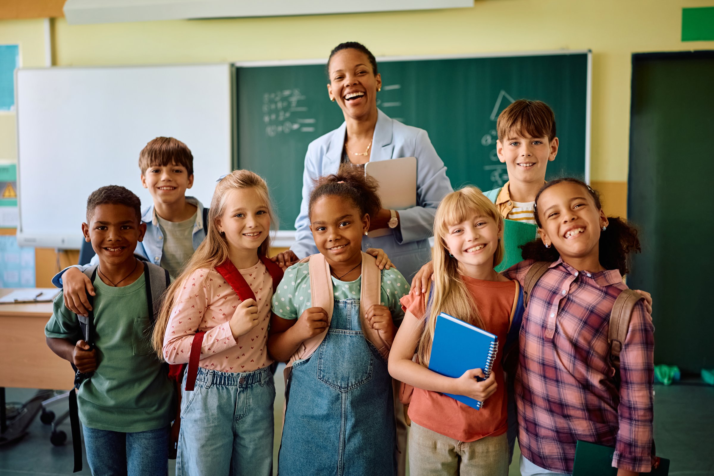 Happy African American teacher and her students in the classroom at elementary school looking at camera.