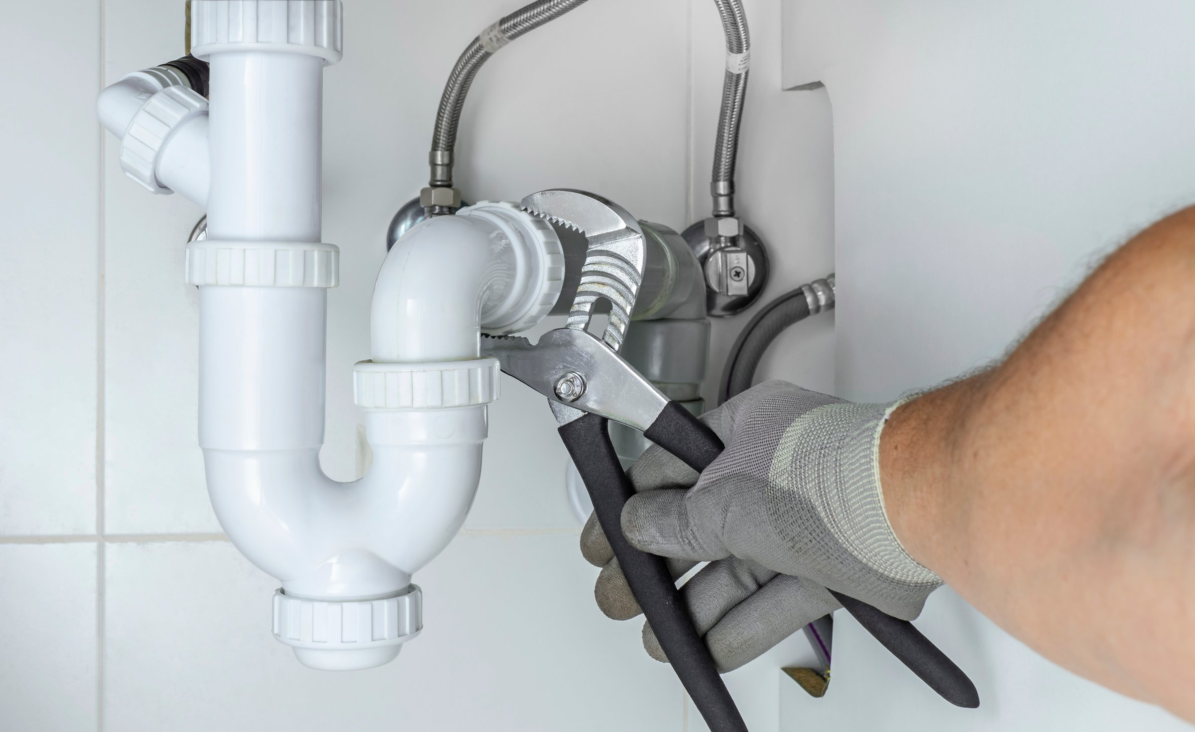 The plumber's hand fixing or unclogging the kitchen sink drain siphon. Home insurance for maintenance and repair water leakages and other emergency breakdowns. Home service guard 24 hours.