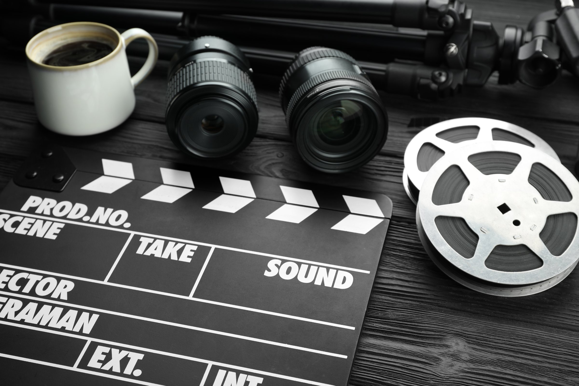 Movie clapper, camera lens, film reels and cup of coffee on black wooden table, closeup