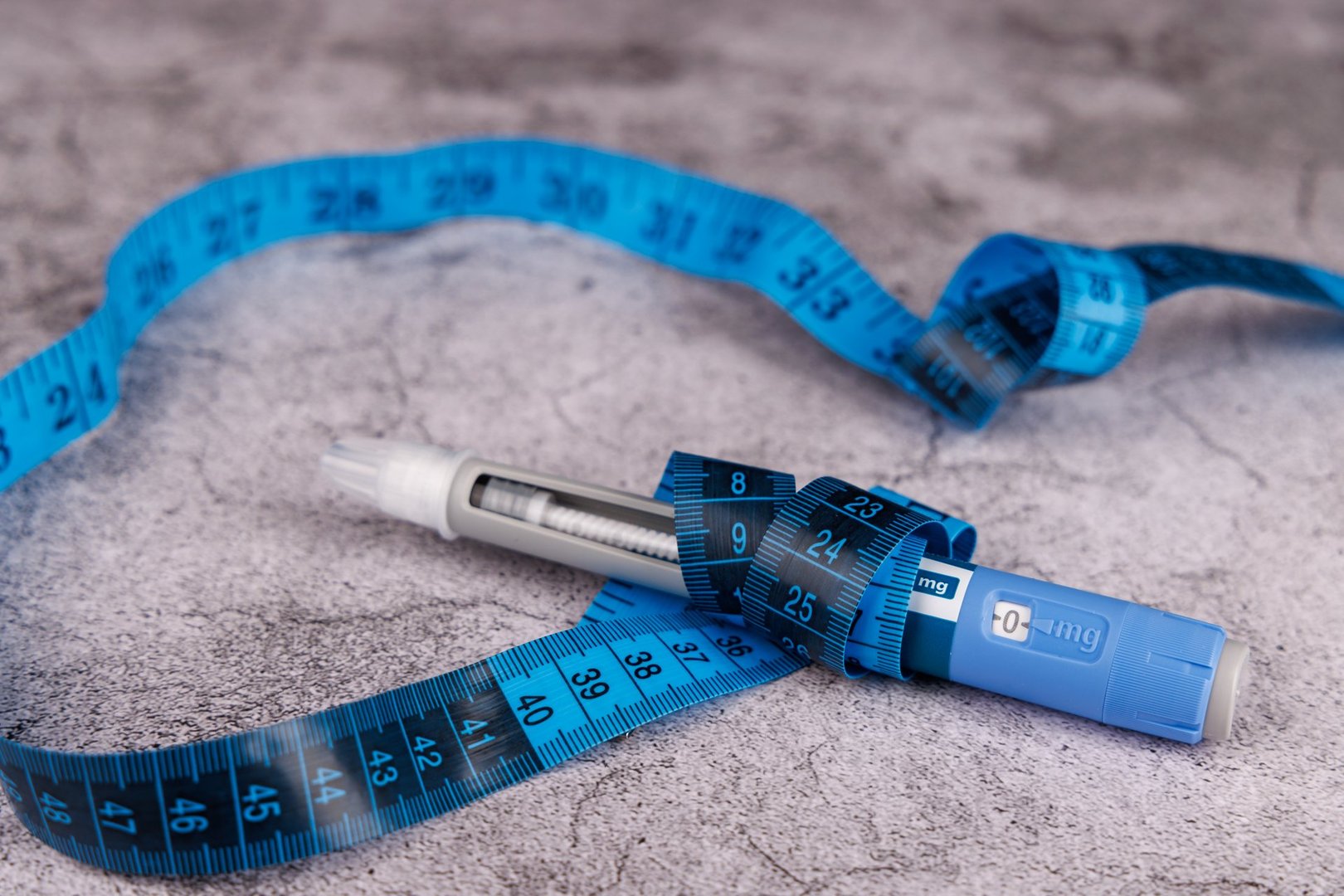 Blue measuring tape, semaglutide glucose control pen, and injection pens placed on a smooth concrete table background.