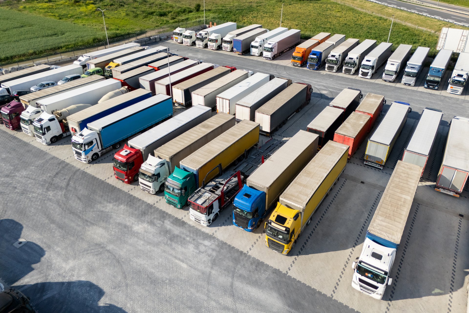 Aerial view of a large truck parking lot at a logistics hub, with multiple commercial semi trucks parked in organized rows.