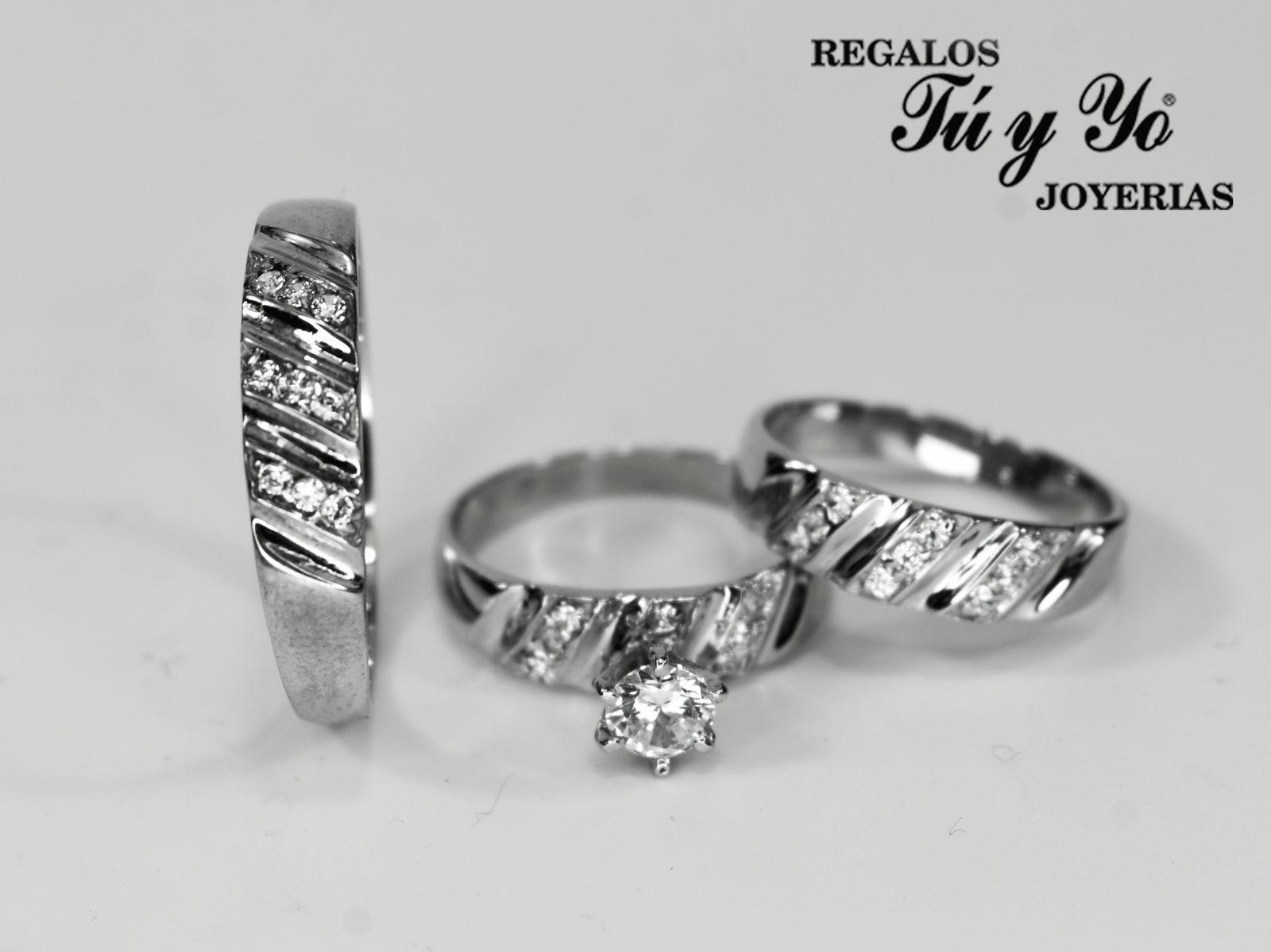 Three silver rings with diamond accents, featuring one with a prominent central diamond. Branding text in the background.