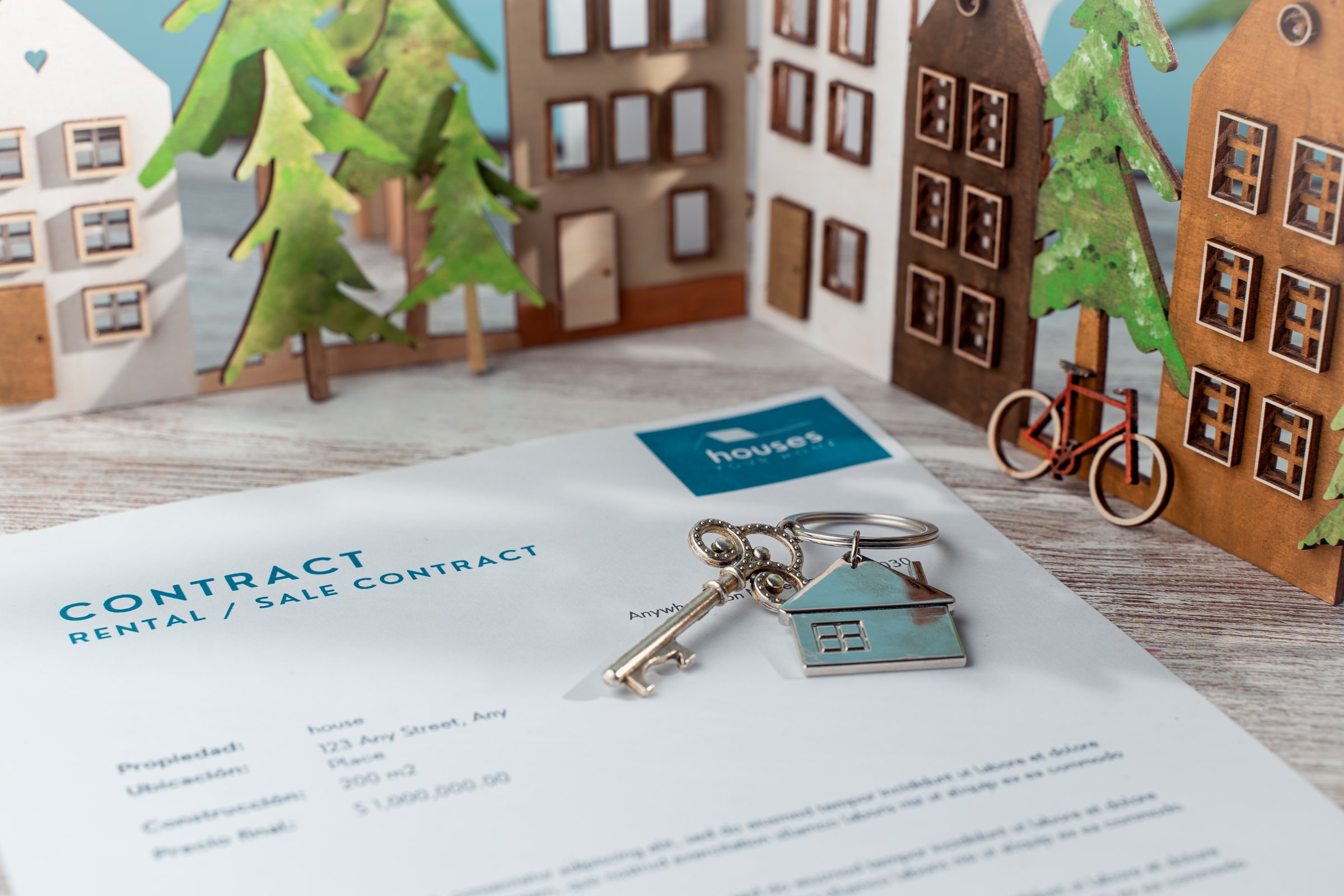 contract of sale or rental of houses with keys and a model of houses in the background.
