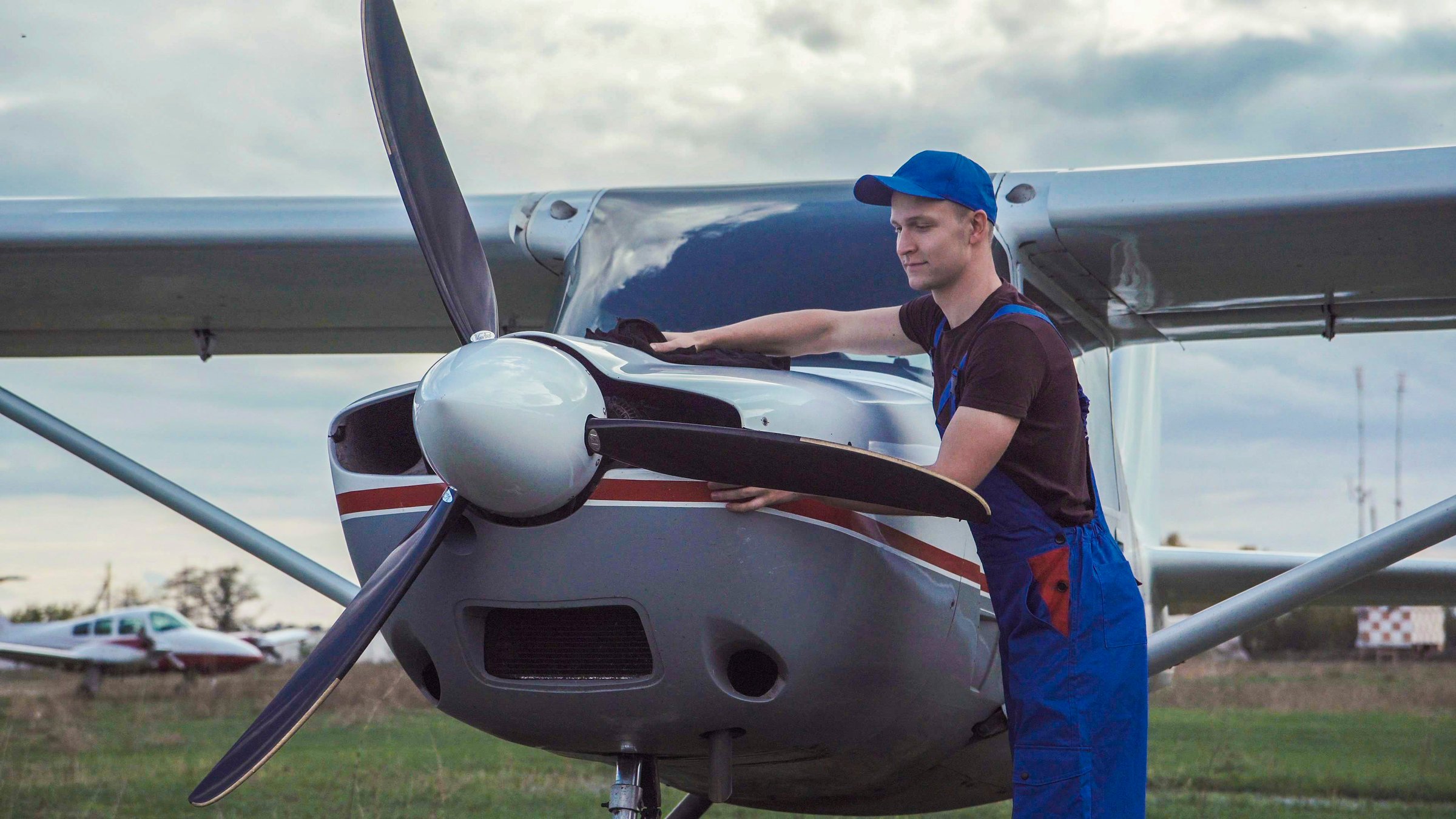 Young pilot or mechanic working on an aircraft wiping down the nose cowling on a small plane parked outdoors on an airfield