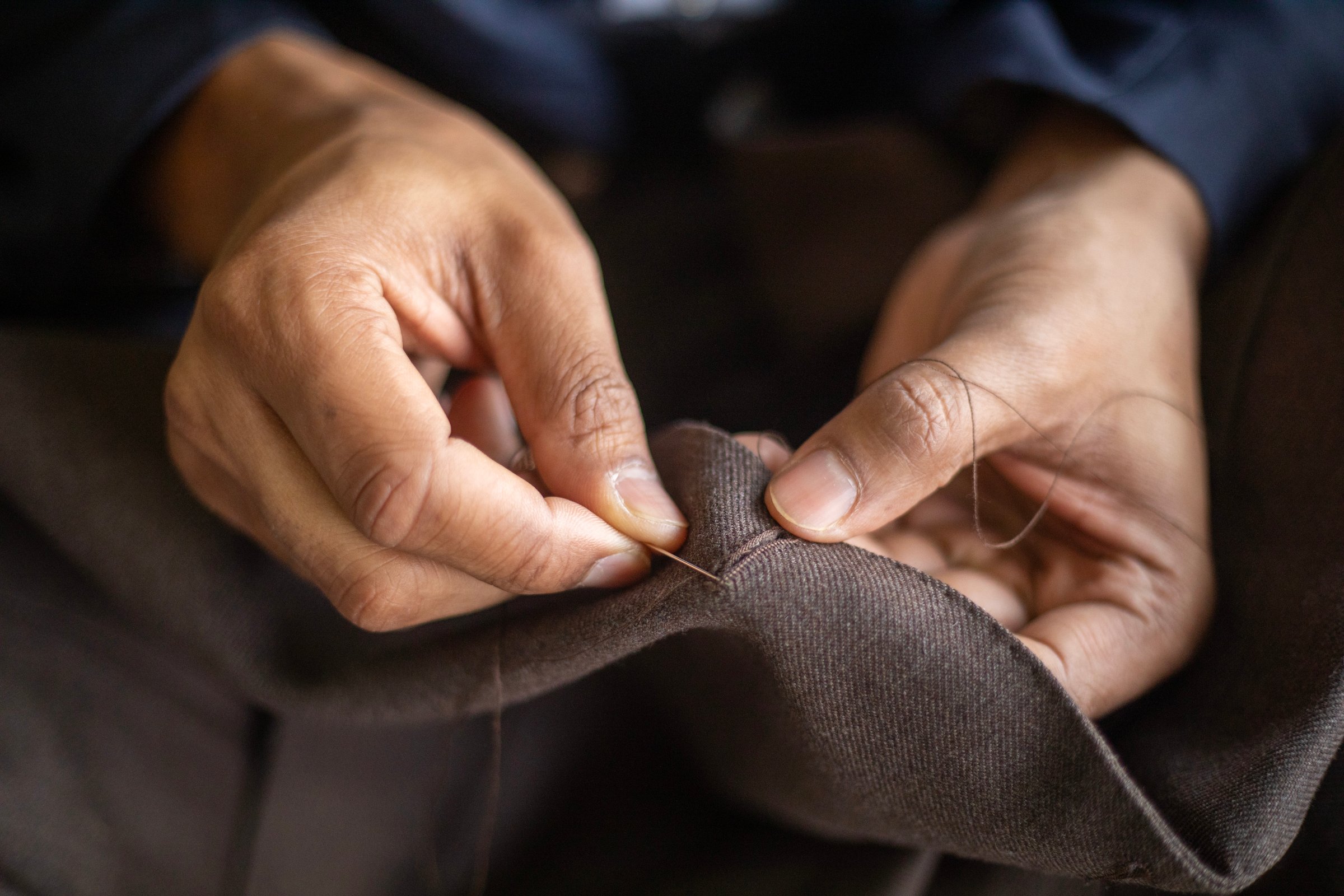 Close up of skilled tailor hand sewing a button hole on a bespoke jacket