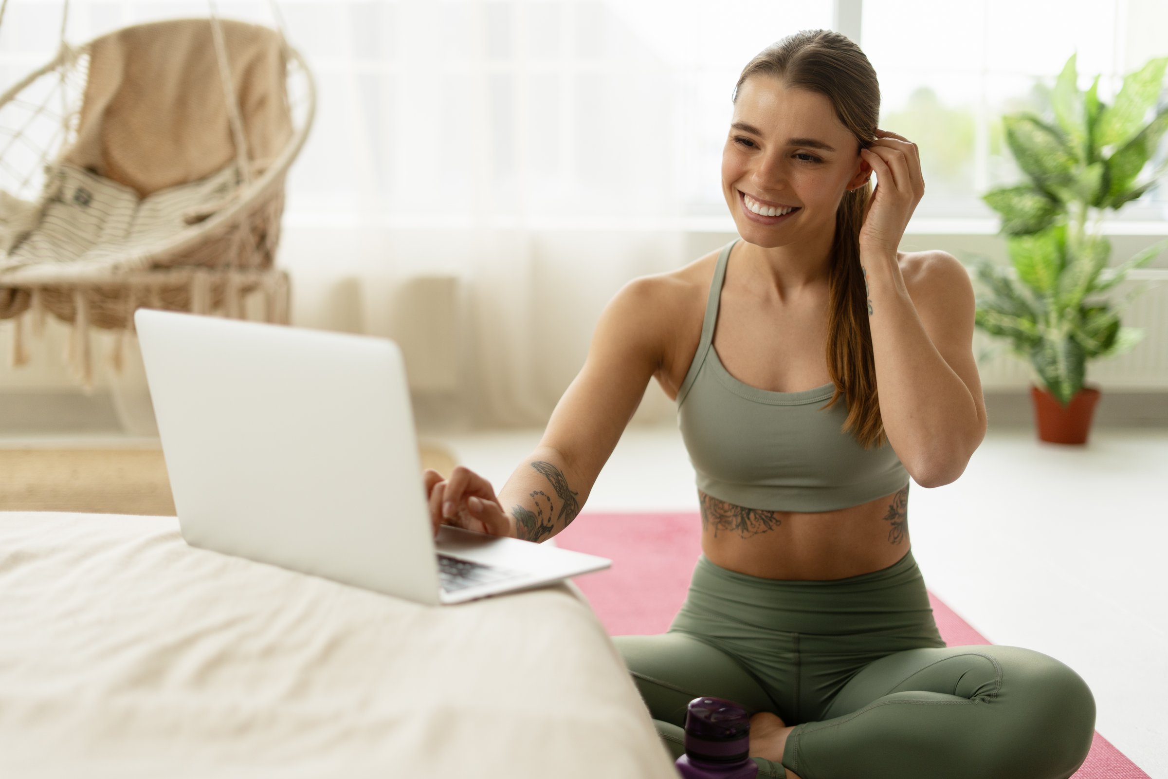 Young woman in sportswear sitting on the floor with a laptop, enjoying an online fitness class and embracing a healthy lifestyle at home