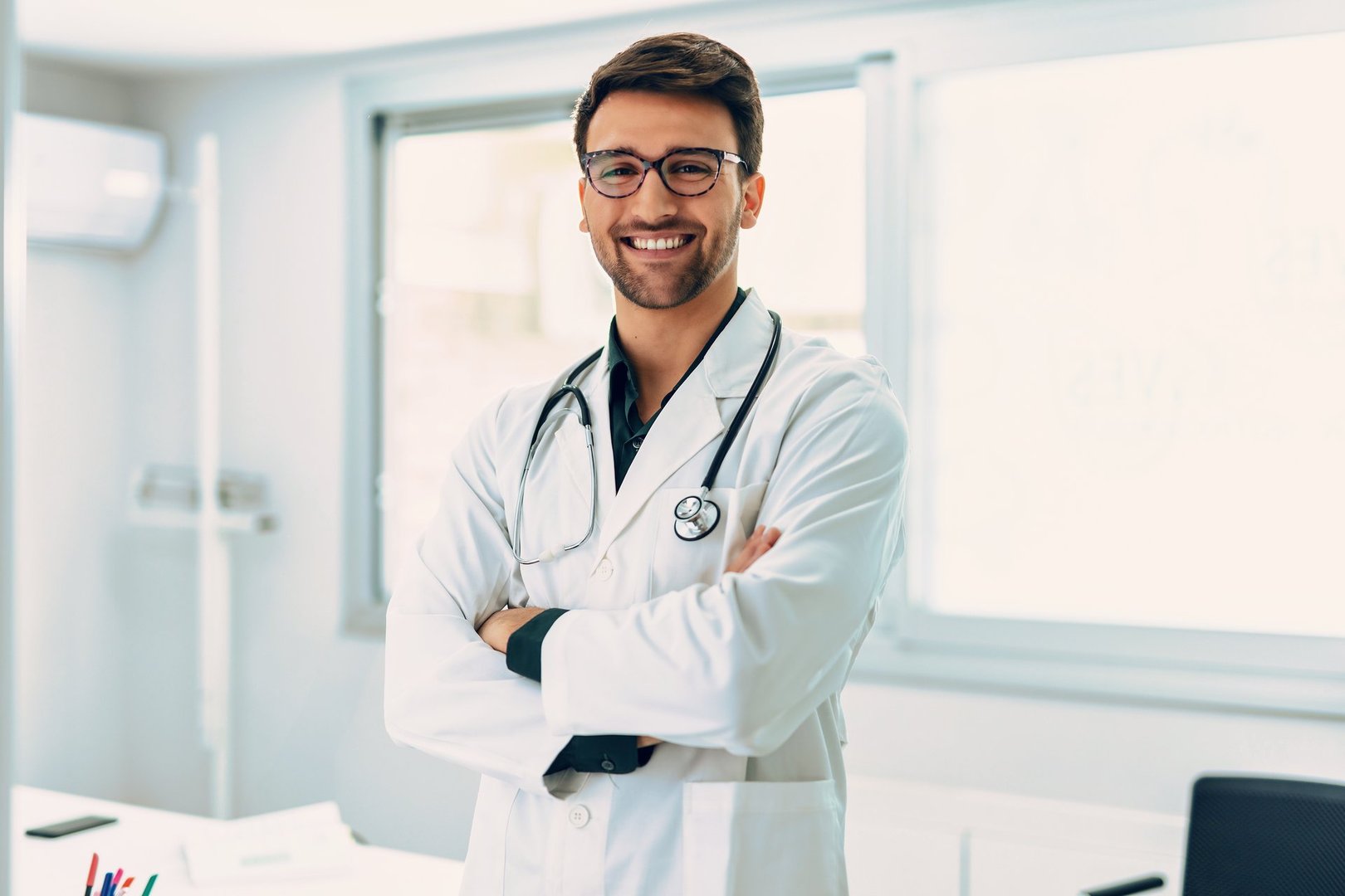Portrait of handsome male doctor with stethoscope over neck working while looking at camera in the medical consultation.