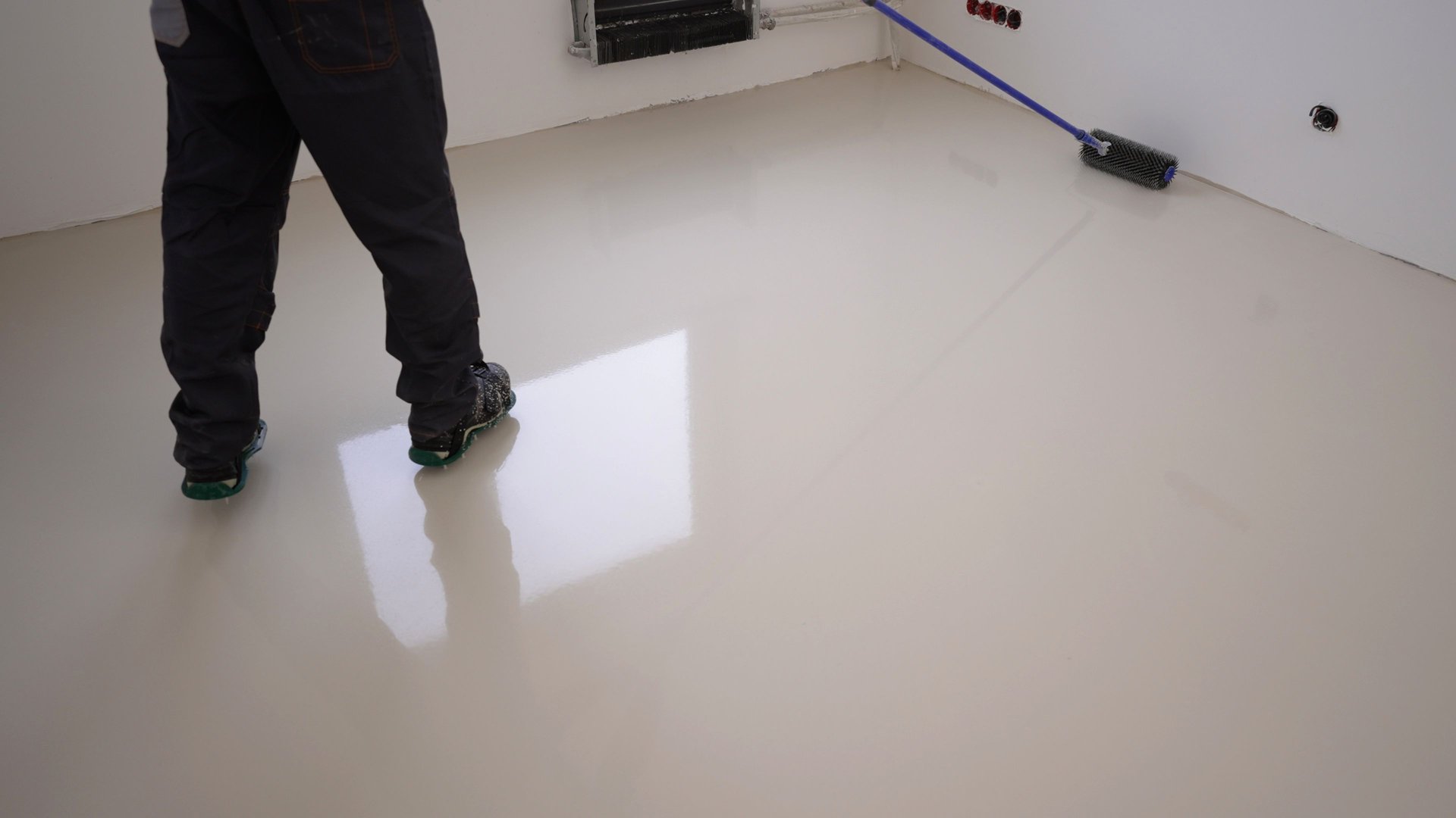 A worker uses a roller to pour the construction mixture onto the floor. Working and needle roller. A worker applies gray epoxy resin to a new floor. A worker with a needle roller applies a new concrete screed with self-leveling cement mortar for floors.