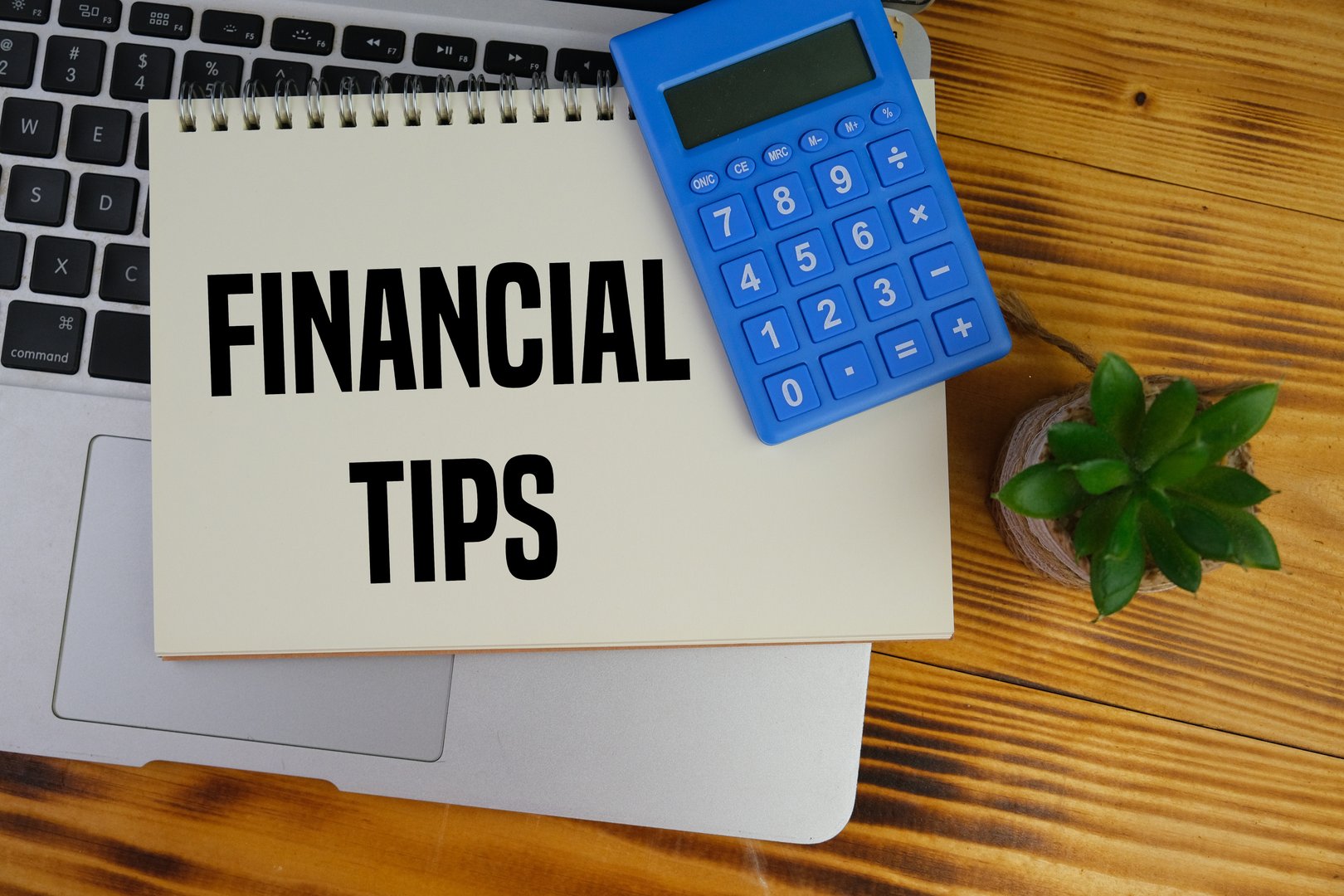 Text of FINANCIAL TIPS with view of a workplace with a laptop, calculator and notebook, on a wooden table. Education, business, Financial and office concept.