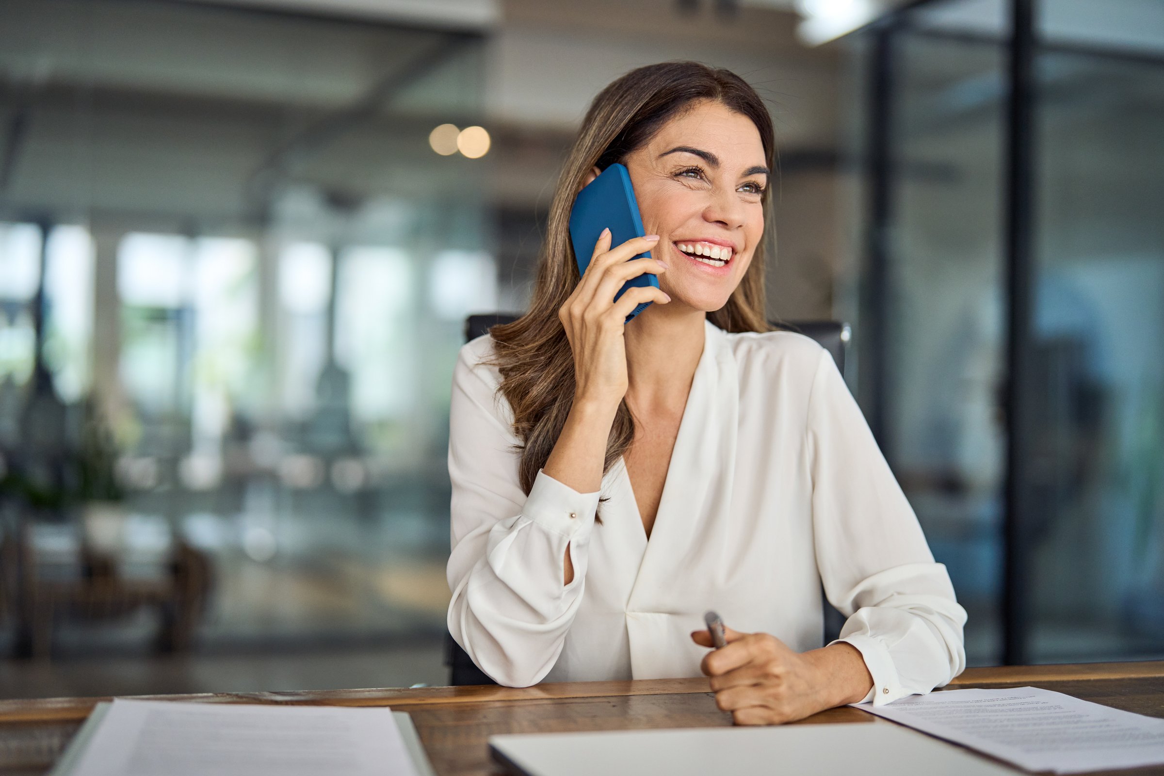 Happy smiling mature mid aged business woman, cheerful 40 years old professional lady executive manager or entrepreneur talking on phone making business call on cellphone at work in office.