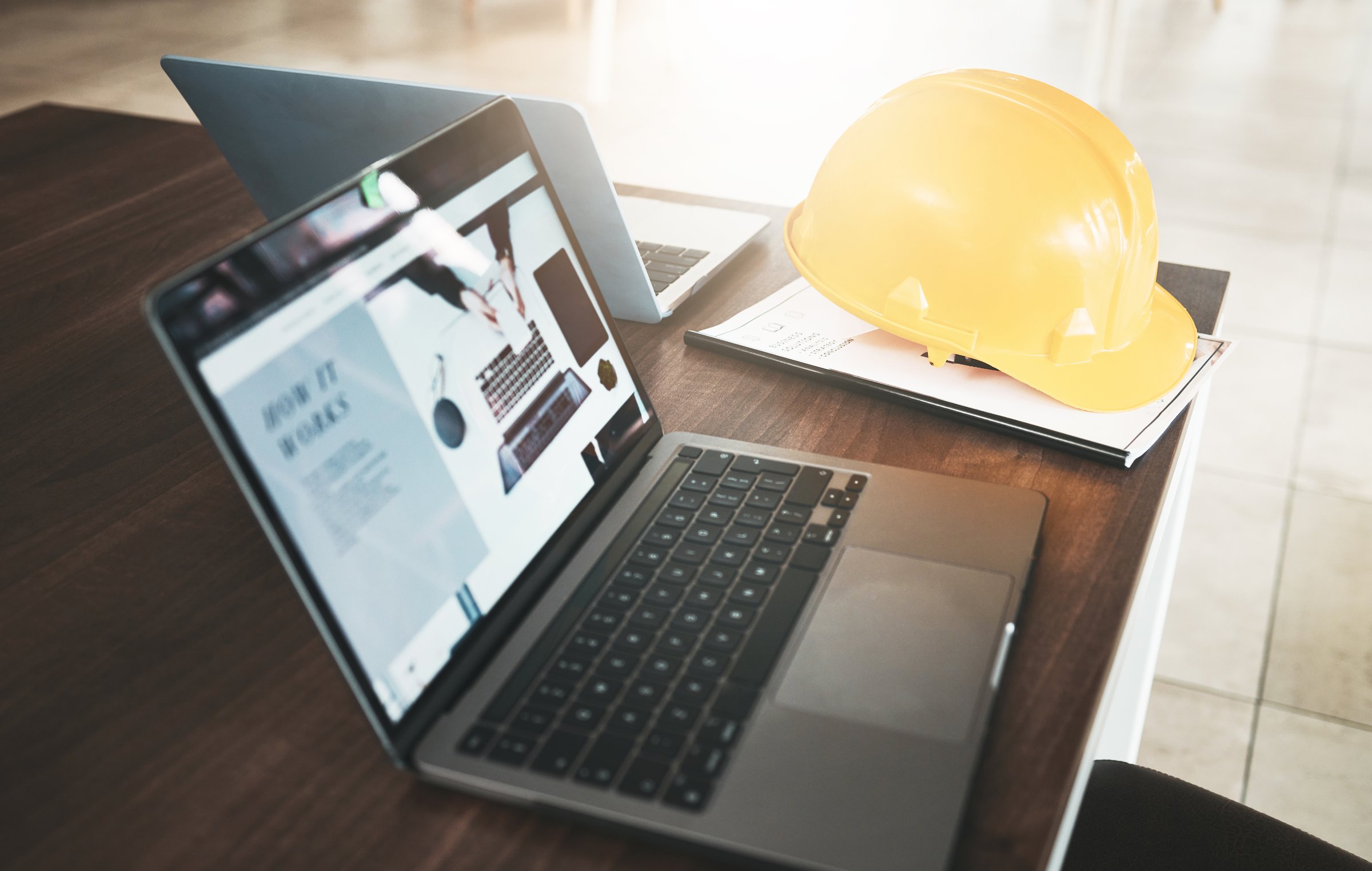 Laptop, hardhat and desk in an industry office for engineering architecture project planning. Industrial, construction and computer or technology for research with a safety helmet in the workplace.