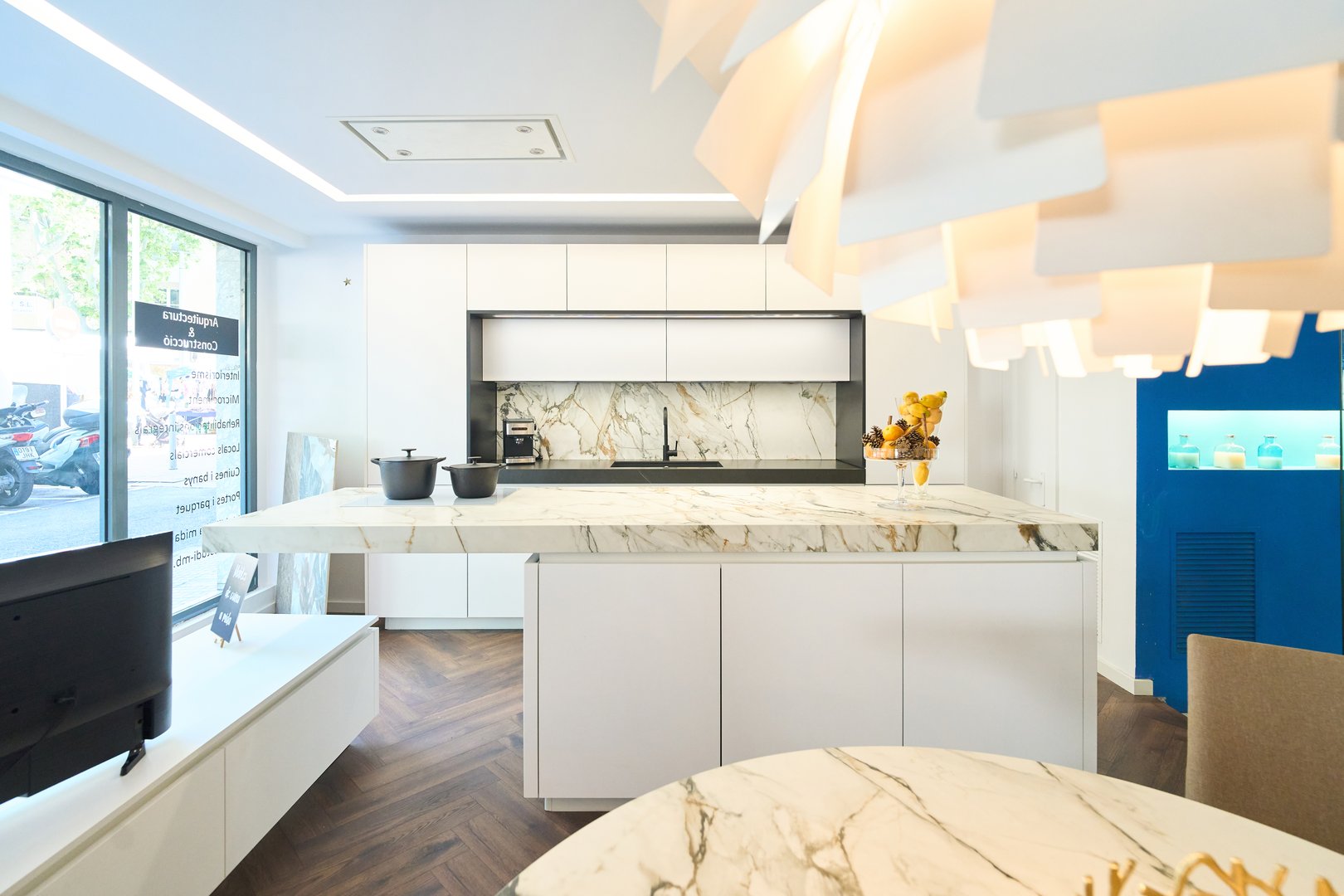 Bright, contemporary kitchen showroom featuring marble countertops, white cabinets, and a stylish designer light fixture