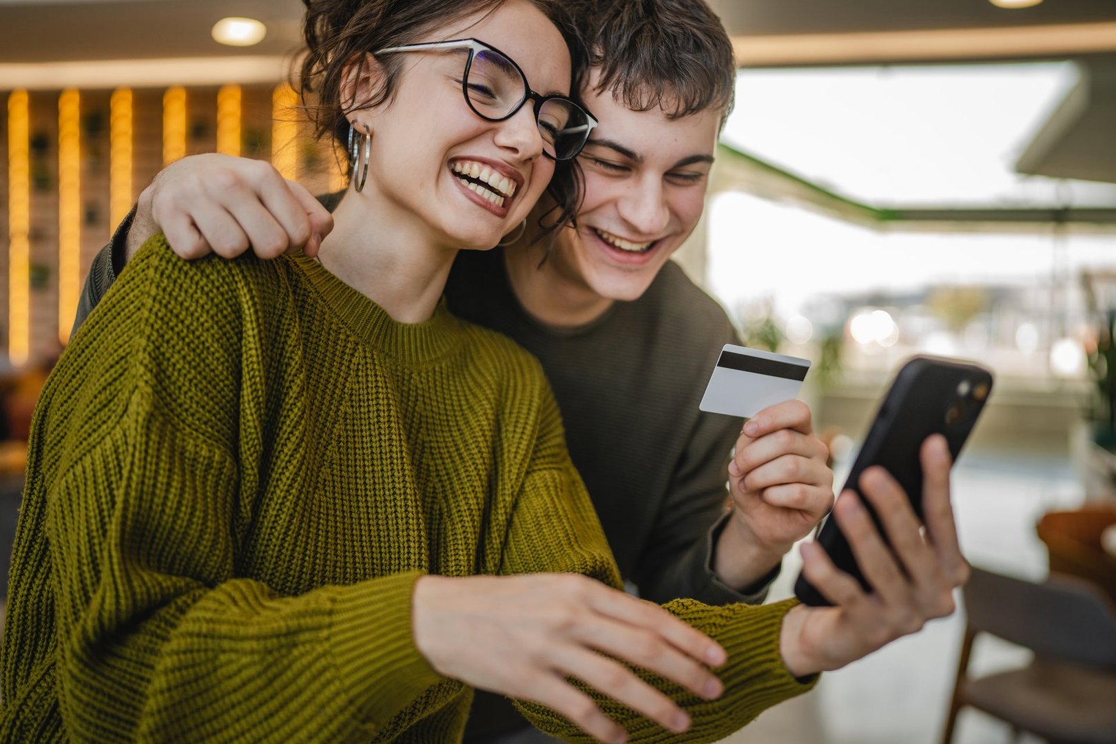 young happy couple use credit card for online shopping on mobile phone at cafe