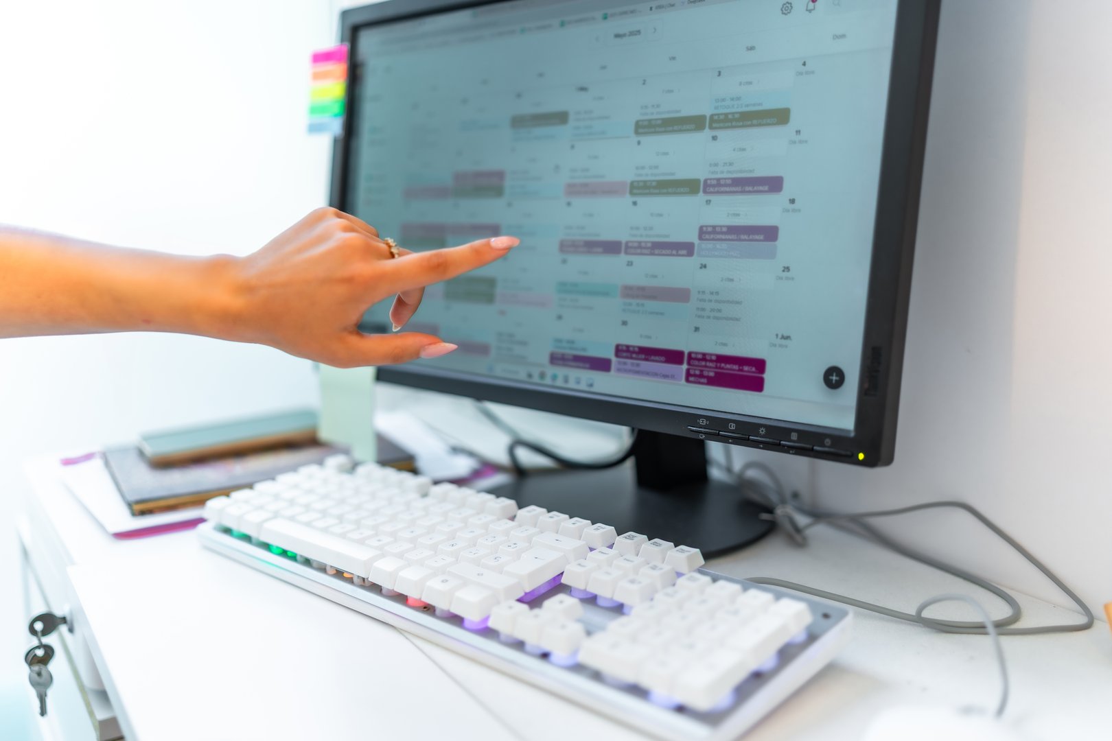 Beautician pointing at a computer screen with an appointments calendar while managing scheduling tasks in a busy beauty salon