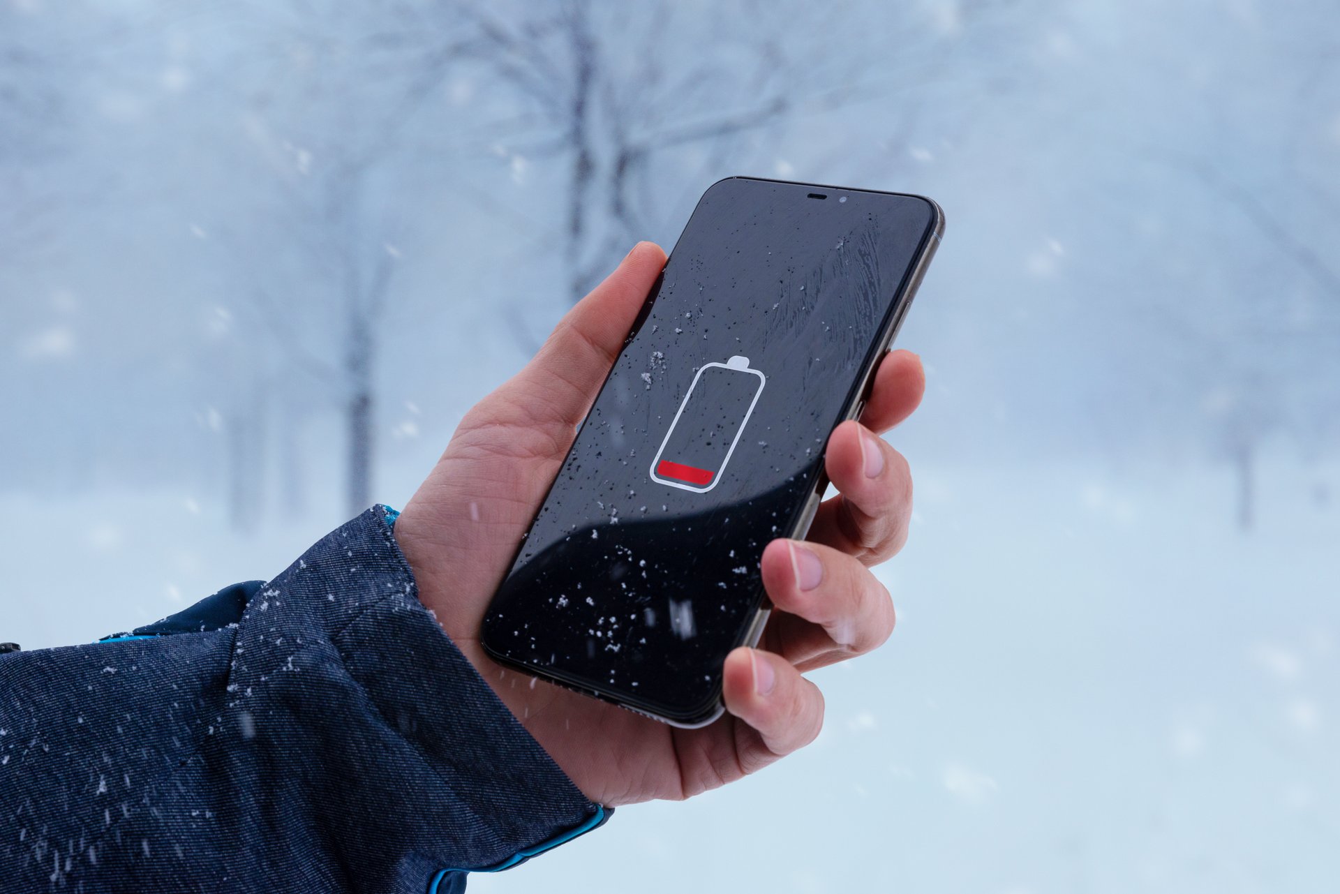Low battery on smartphone in man hand. Winter, cold time.  Concept of faster battery discharge at low temperatures