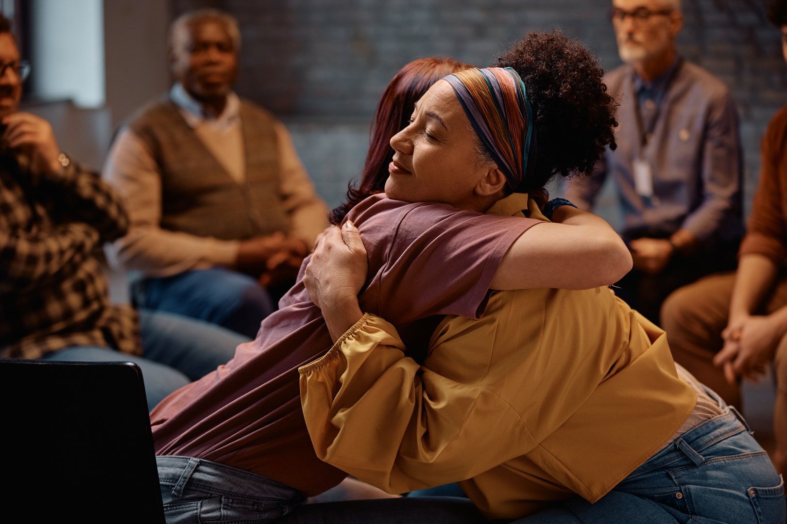 Group therapy participants hugging during mental health counseling at communicating center.