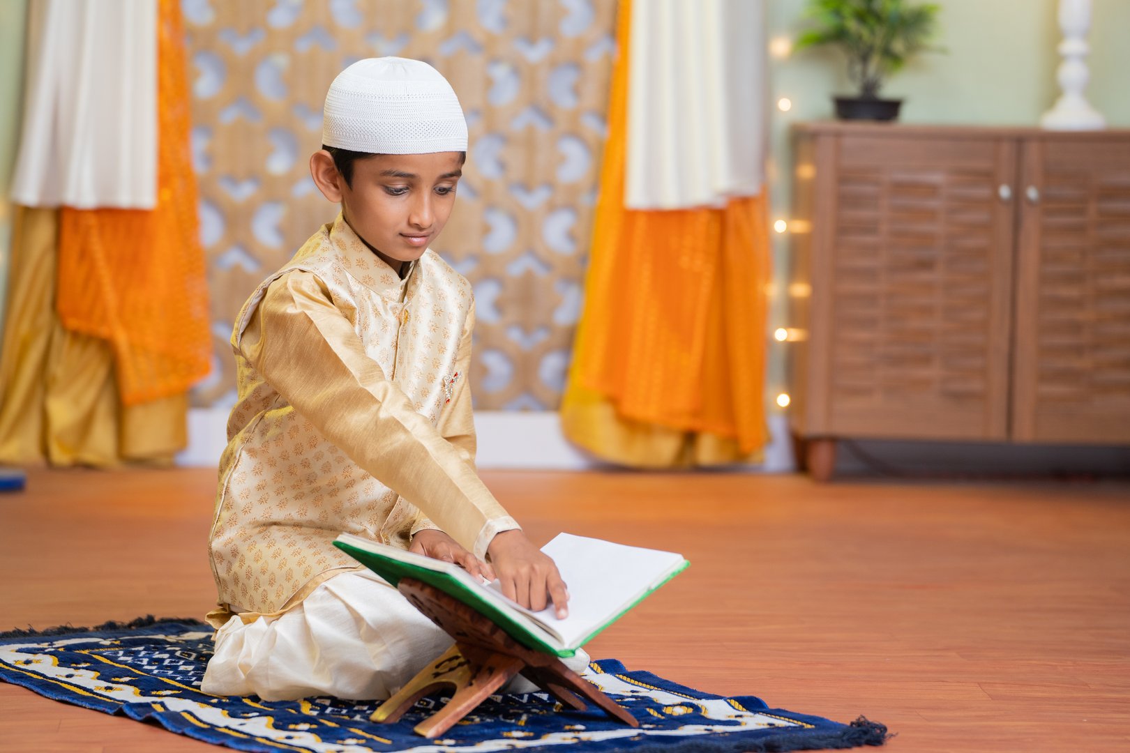 Young teenager Muslim boy reading Quran book during Ramadan feast celebration at home.