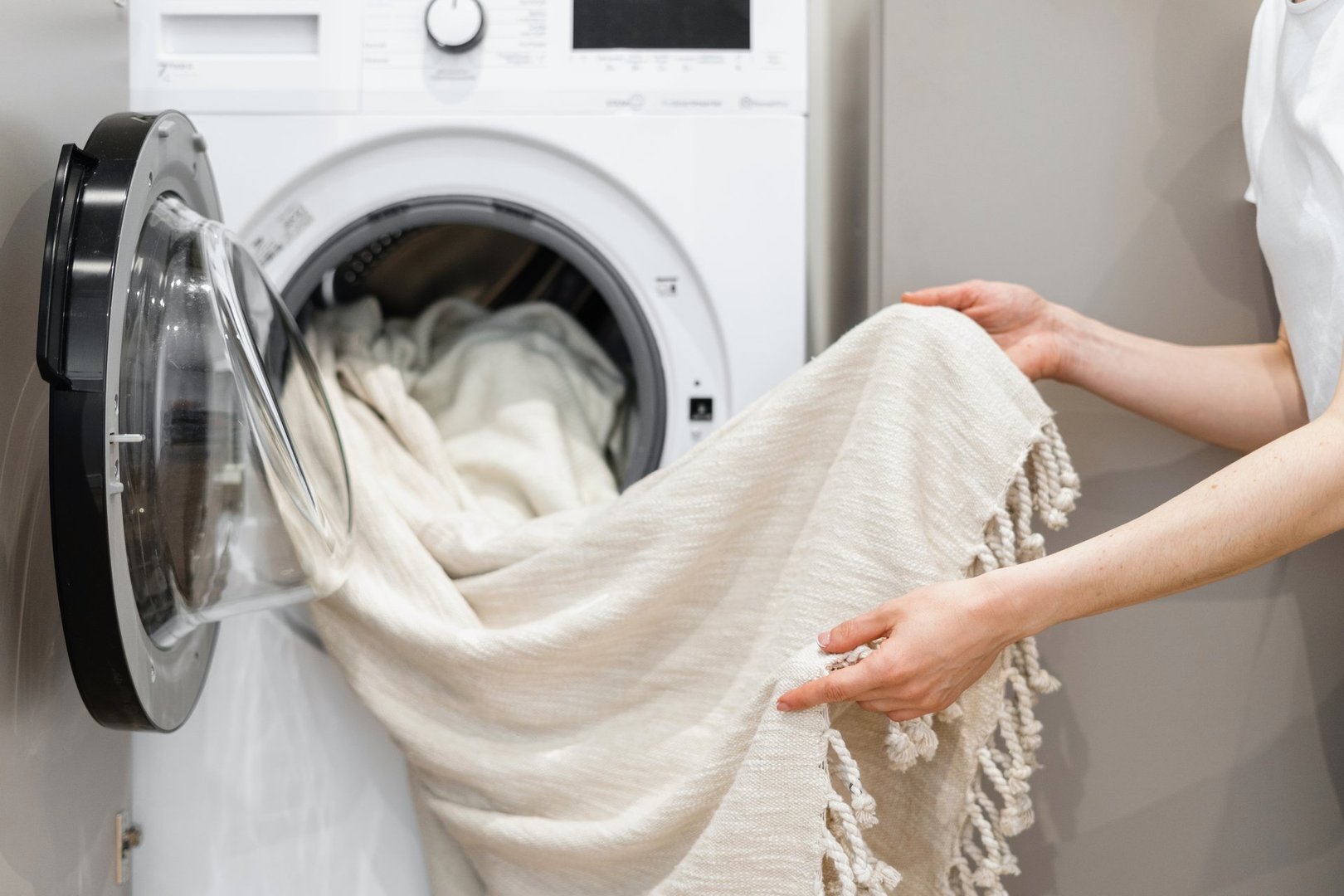 Cropped view of woman unloading laundry from white washing machine. Tulle cleansing. Cleaning service worker. Concept of purity. Housekeeping idea