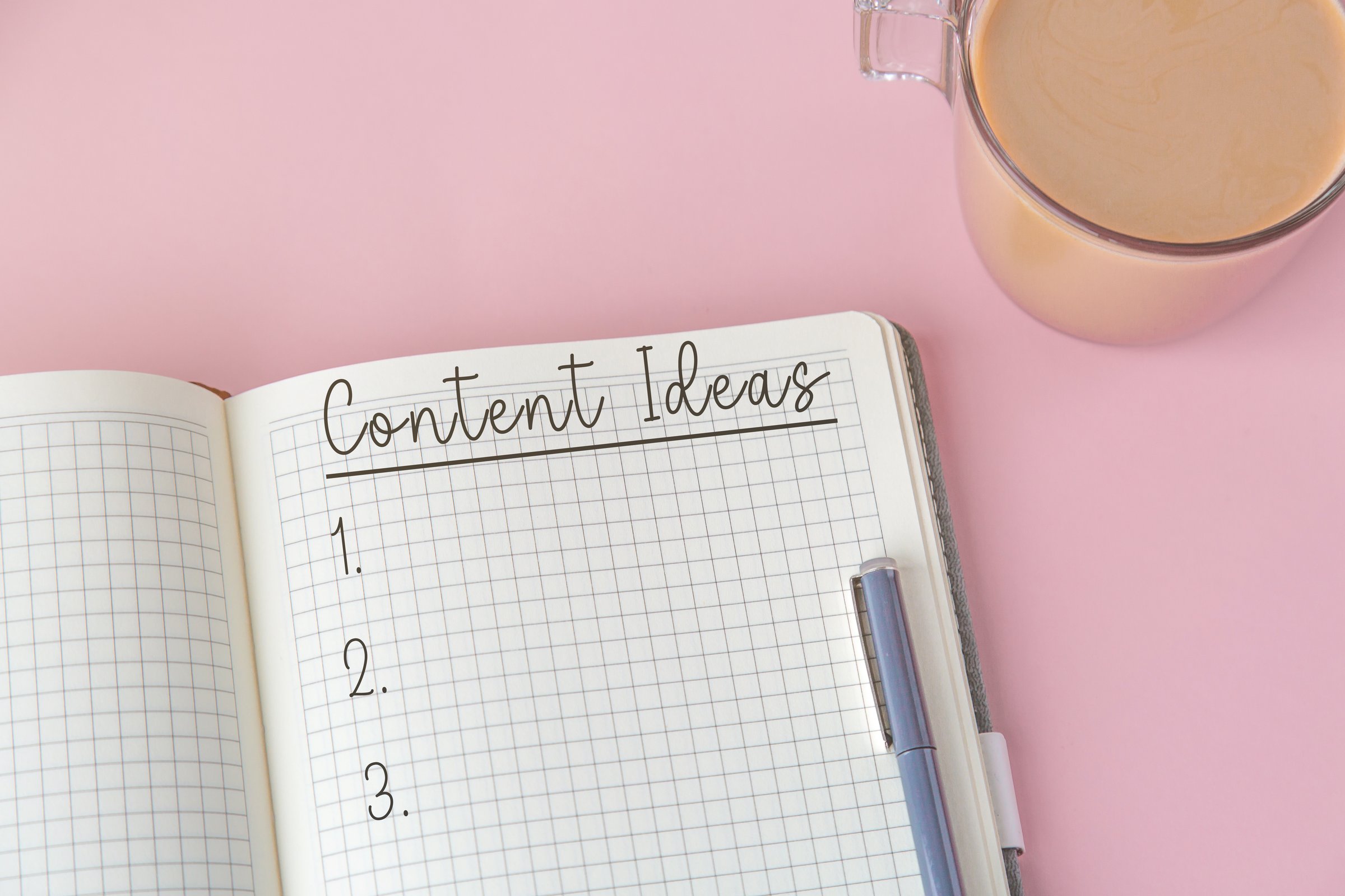 Open notebook with handwritten title text Content Ideas, blue pen and cup of coffee on pink background, flat lay for blogging or planning, creativity and productivity concept