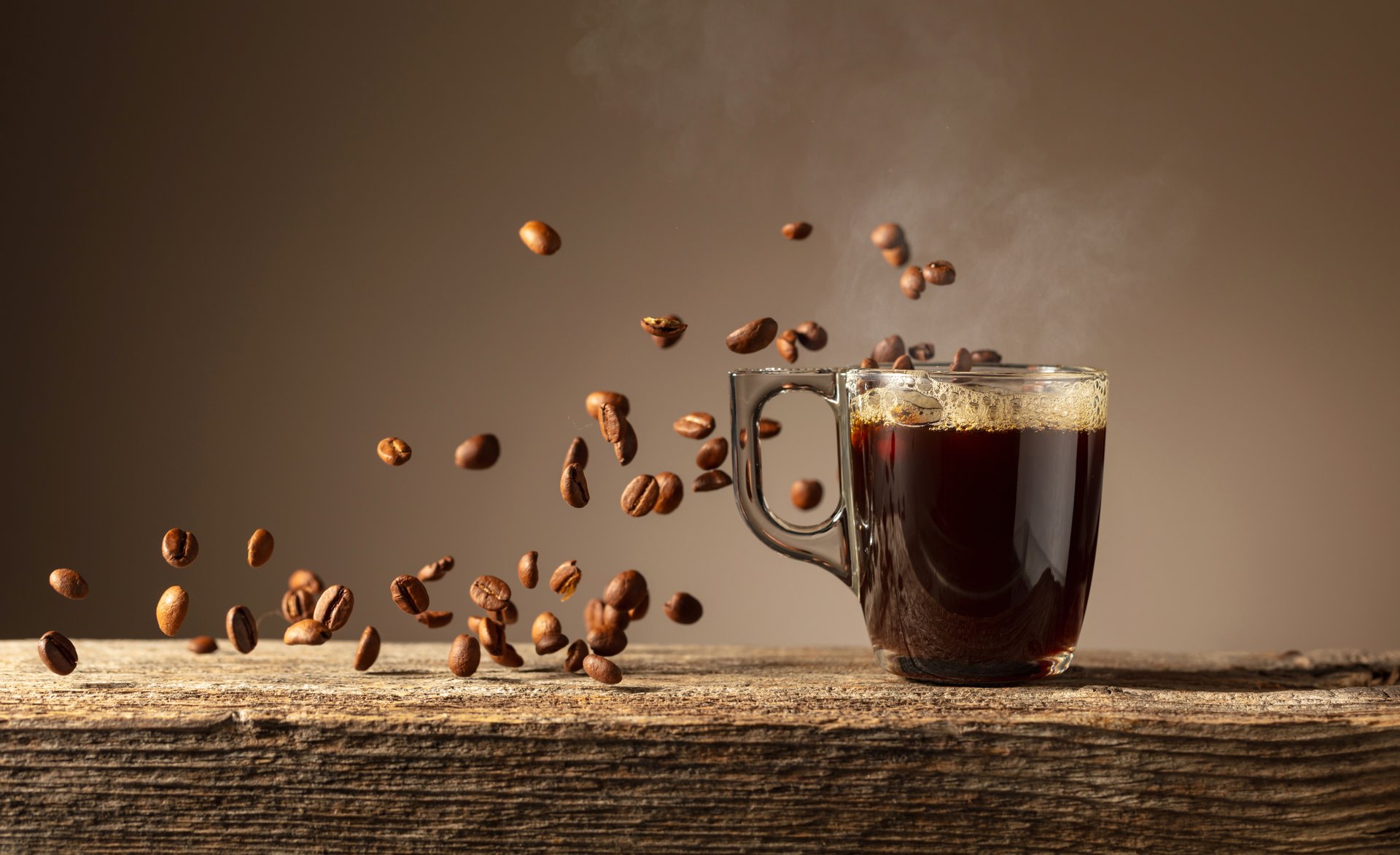 Espresso in glass cup on a old wooden table. Roasted coffee beans in motion. Copy space.