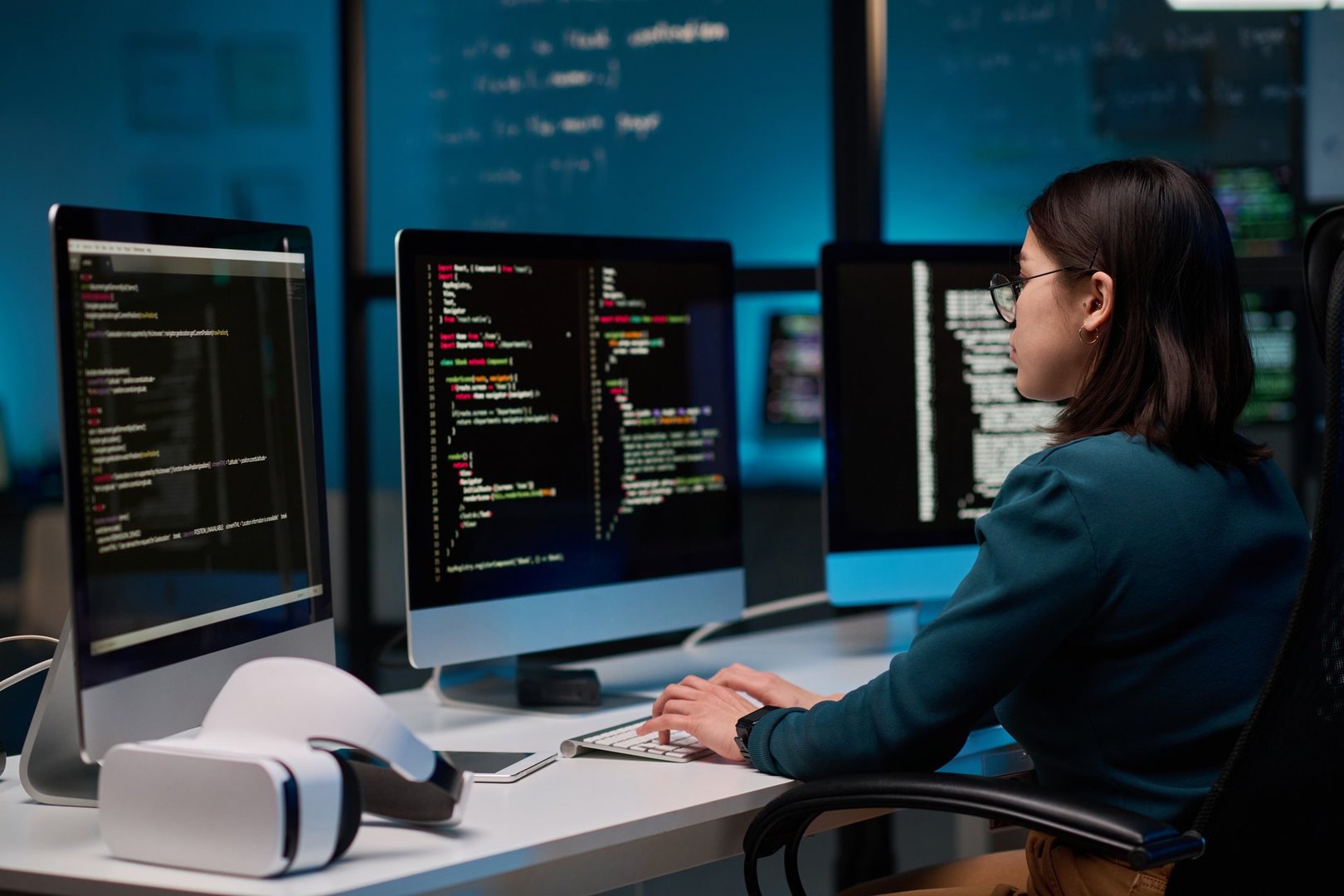 Female IT developer writing code for VR project at office workplace with focus on computer screens copy space