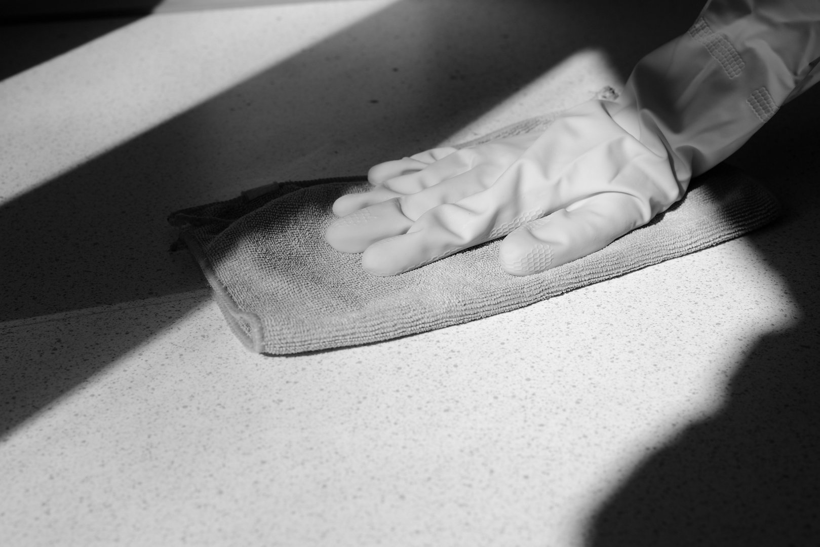 Hand in rubber glove washing surface on a sunny day. Spring cleaning black and white