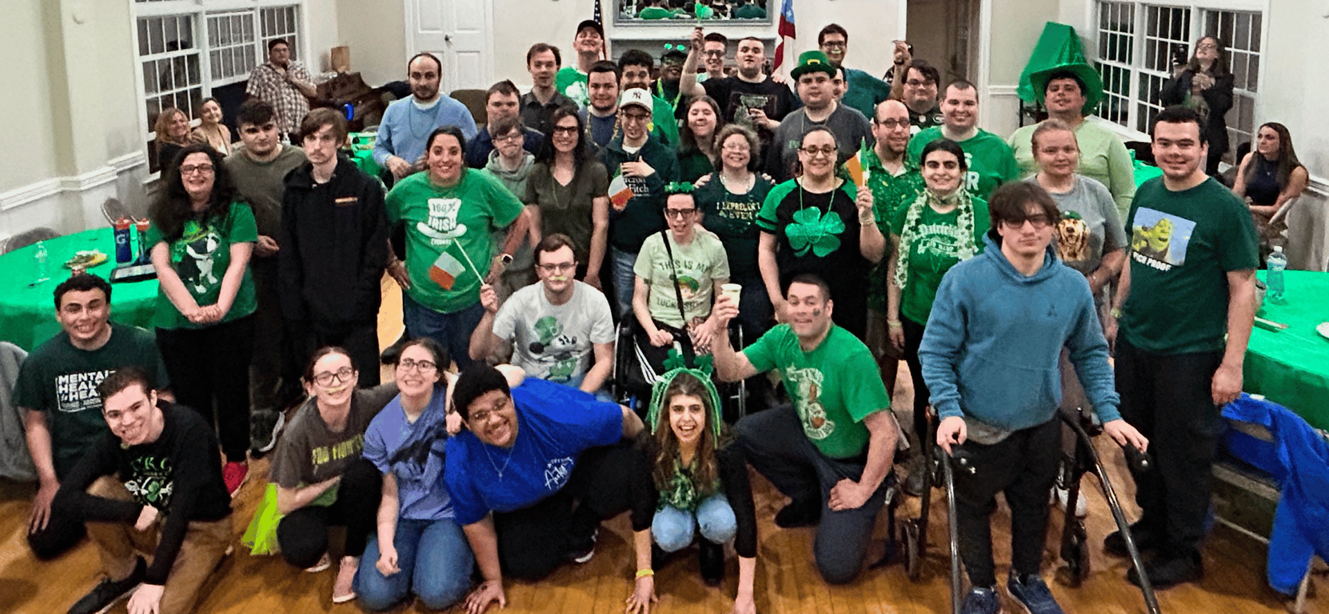 Group photo of people in green outfits celebrating St. Patrick's Day indoors, with festive decorations and smiles.