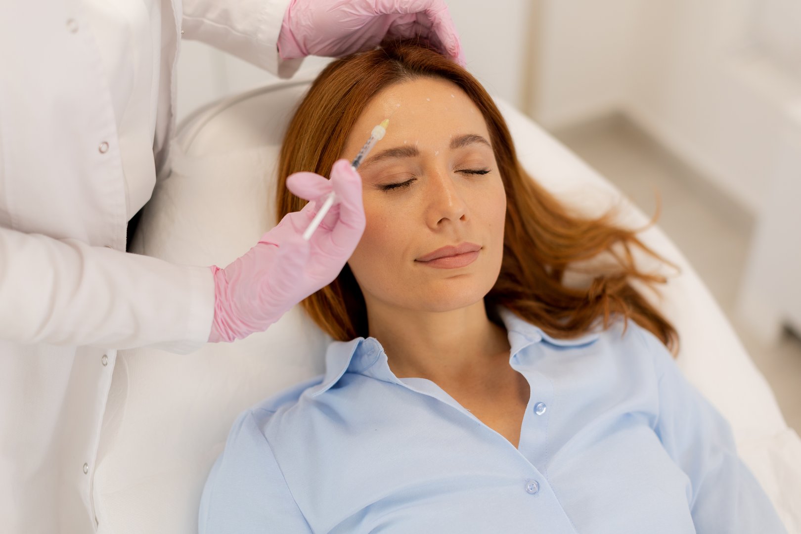 Patient relaxes on a comfortable treatment bed while a skilled practitioner applies dermal filler to enhance facial features in a tranquil clinic environment.