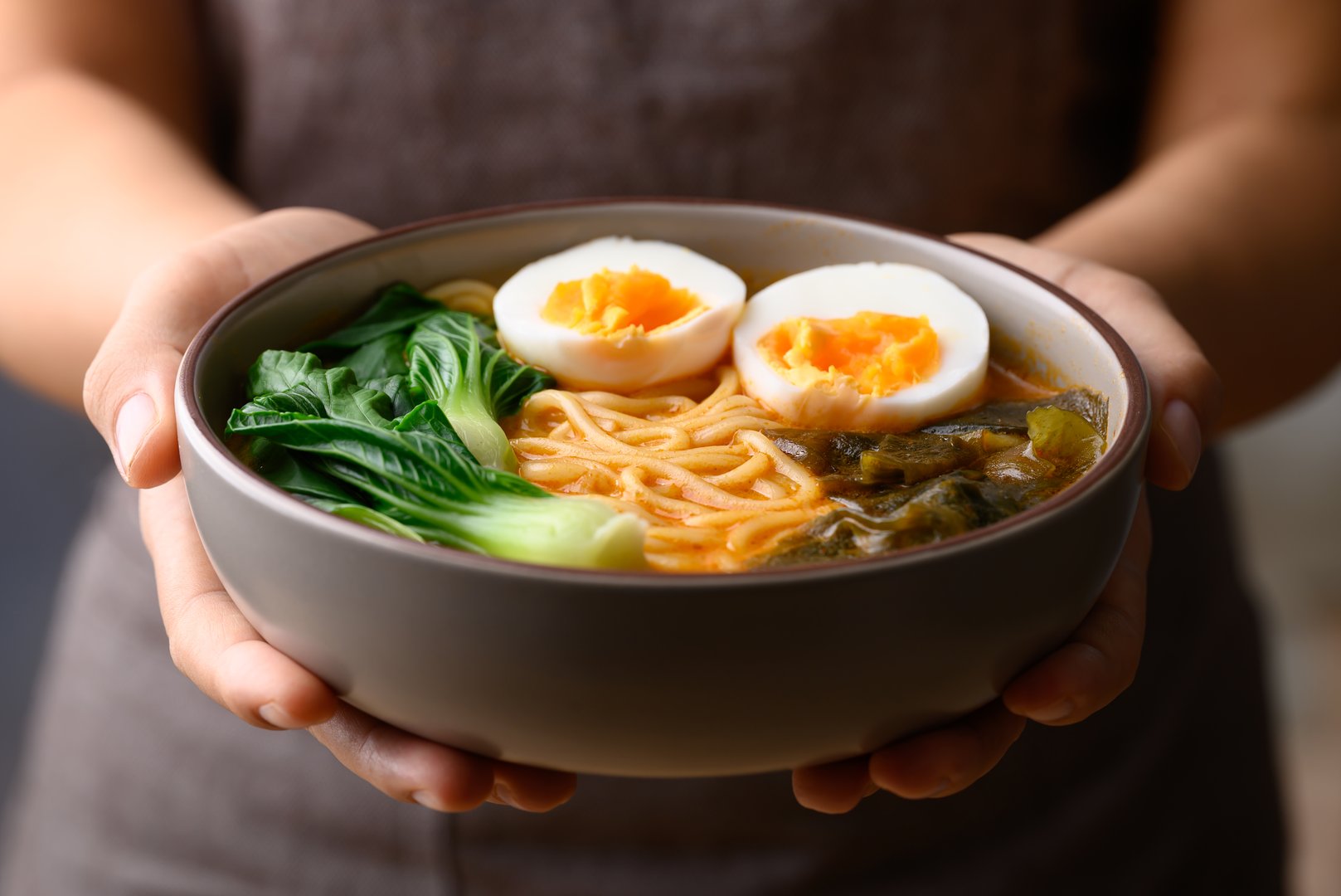 Spicy noodles soup with egg, seaweed and bok choy in bowl holding by hand, Asian noodles style