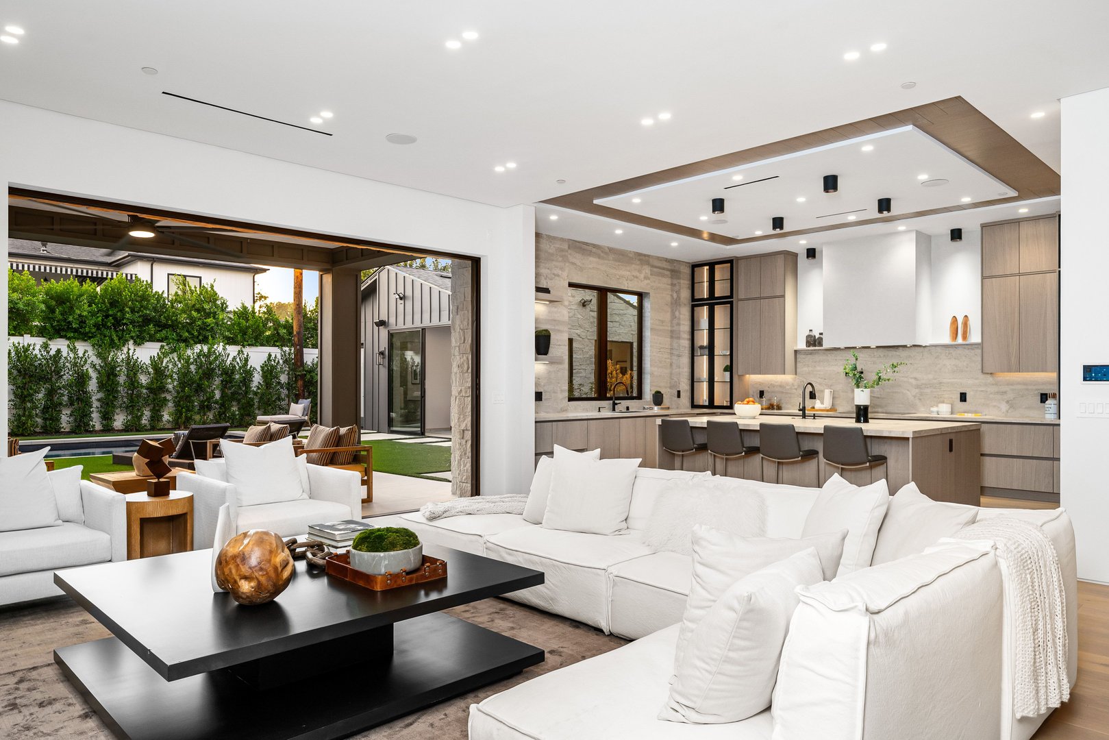 Modern open-plan living room and kitchen with white sofas, sleek design, and outdoor view.