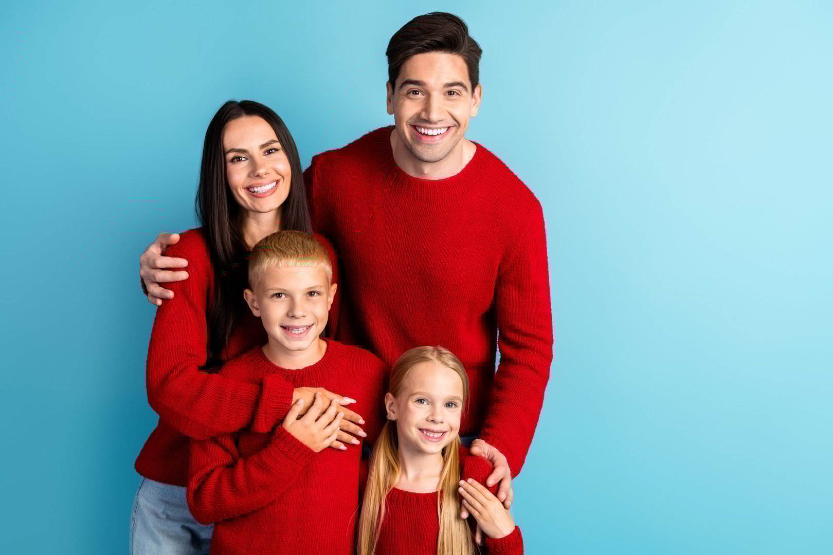 Smiling parents and their children in festive red sweaters bonding, creating joyful holiday vibes for Christmas and New Year celebrations