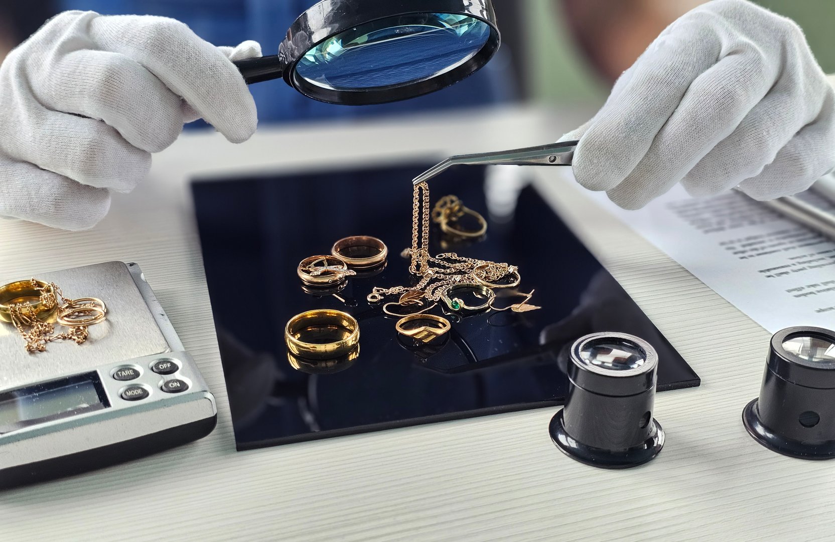 Expert evaluates various gold jewelry pieces with magnifying glass and tweezers in a bright workspace
