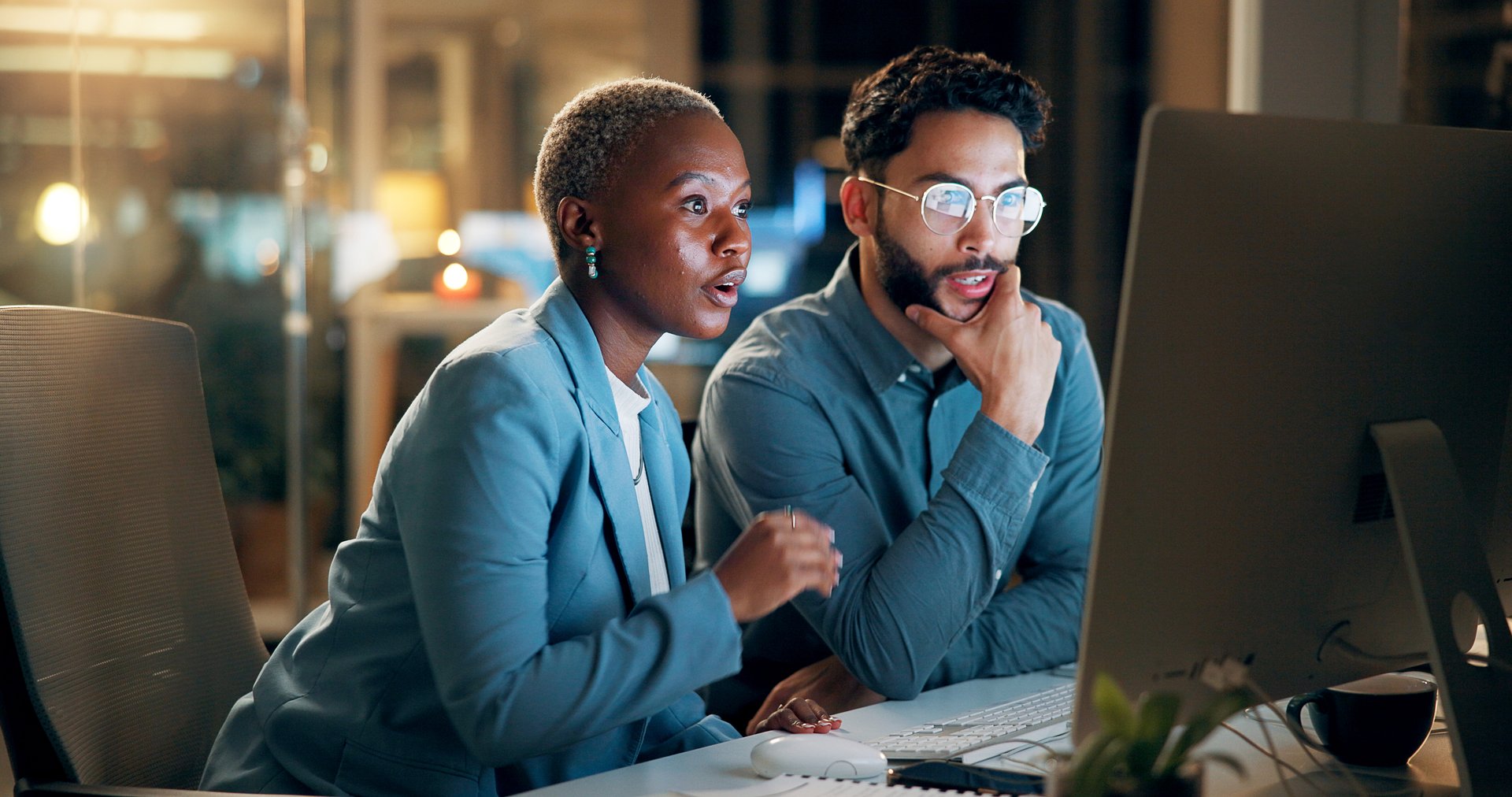 Computer, night and thinking with business people in office together for development or planning. Collaboration, feedback or review with employee man and woman in workplace for project management