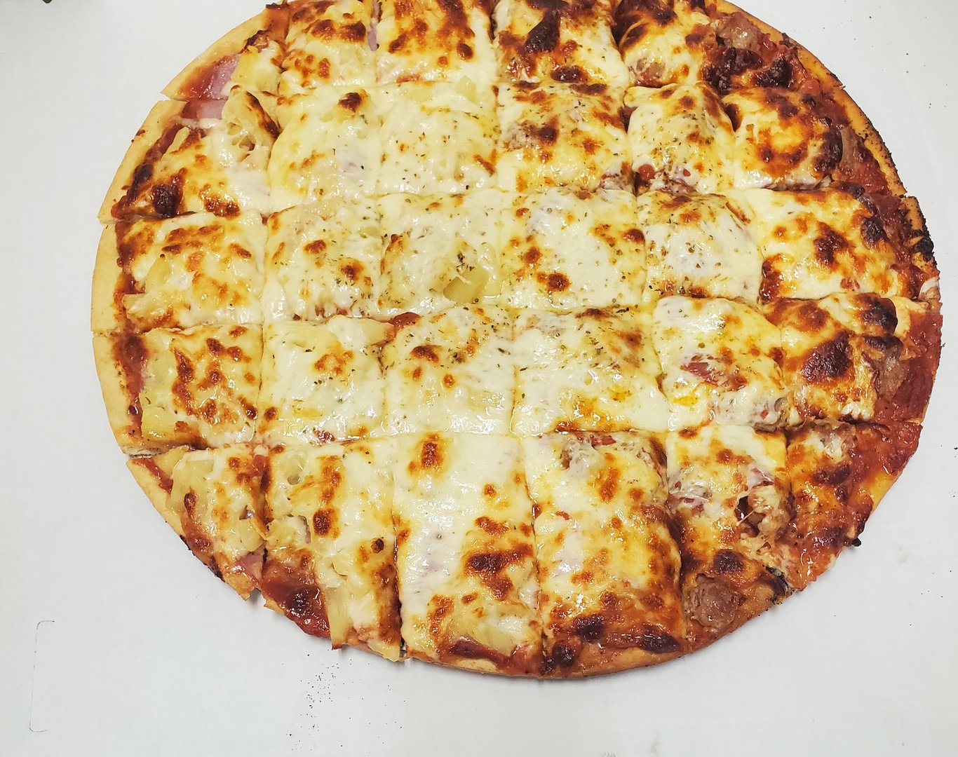 A whole pizza cut into small square slices with melted cheese and toppings, on a white background.