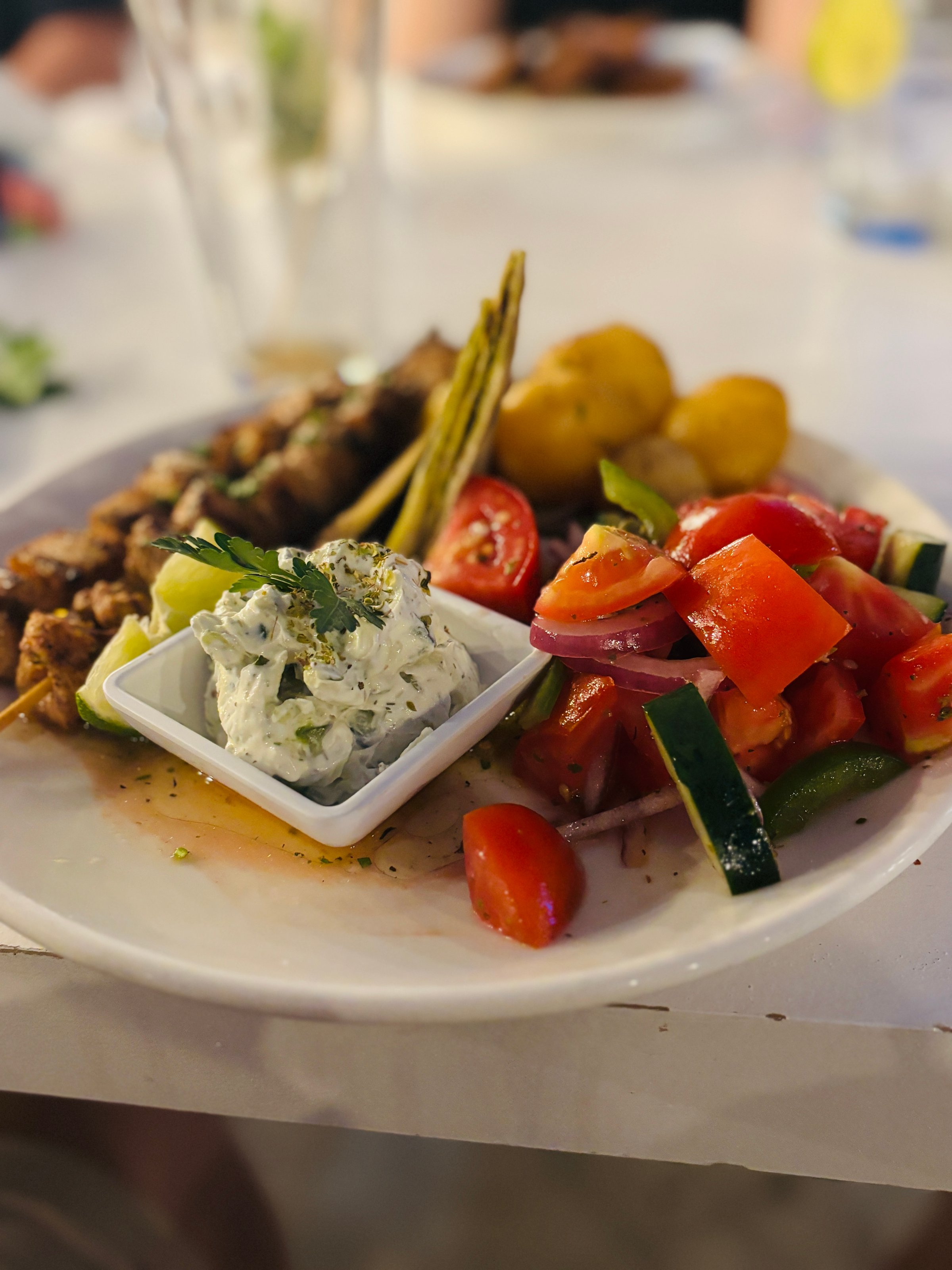 A chicken souvlaki dinner with tzaziki sauce, roasted potatoes and tomato salad.