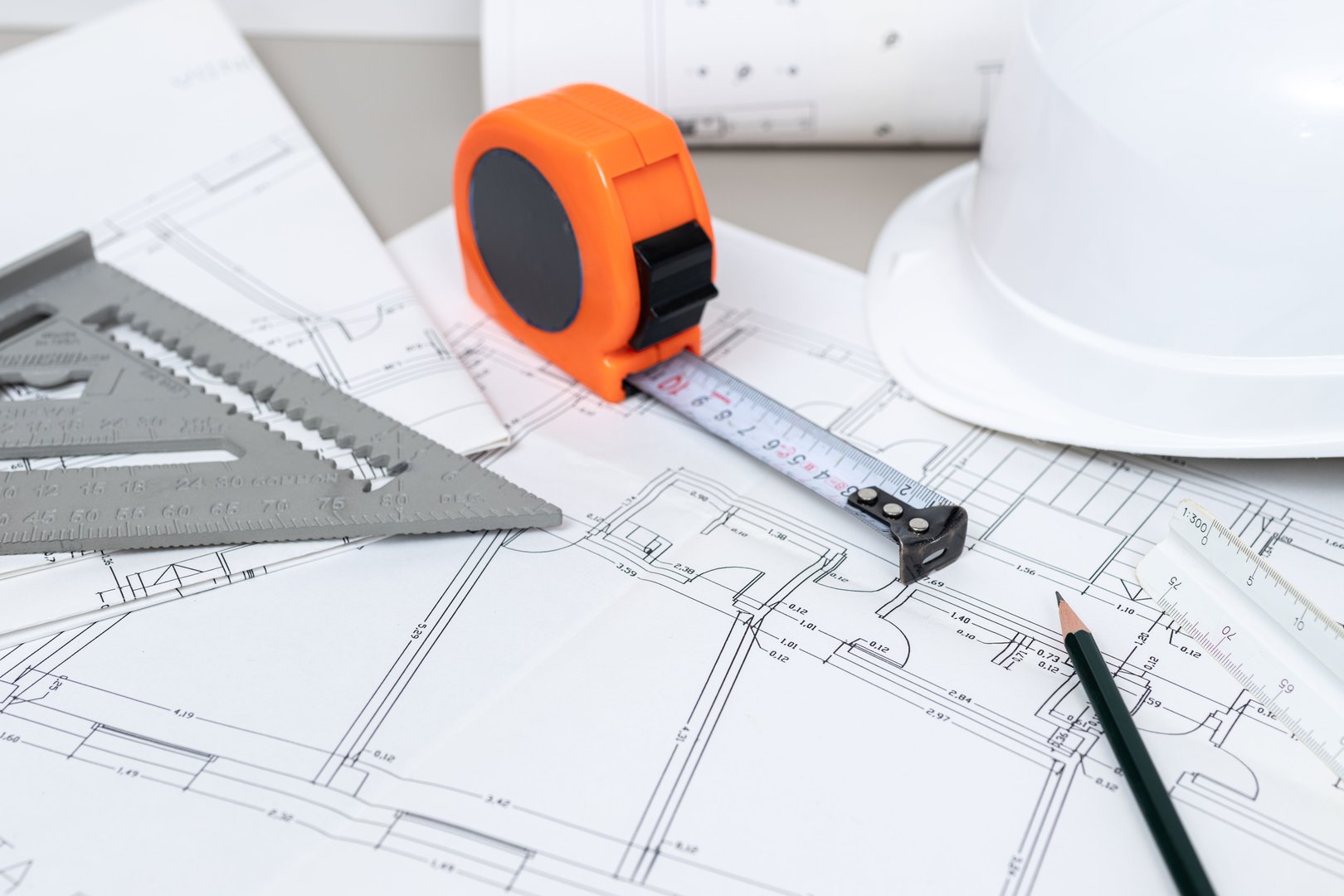 A construction helmet, measuring tape, and rolled blueprints