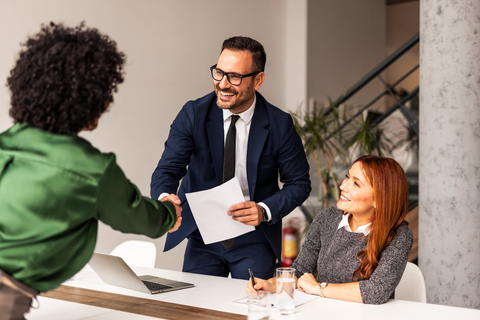 A business team engages in a professional meeting, discussing ideas and shaking hands in a bright and modern office environment. Formal attire emphasizes the productive and collaborative nature of the interaction.