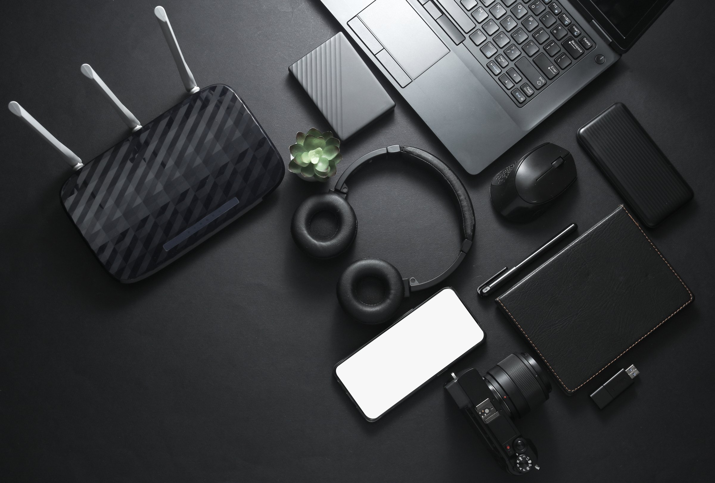 Modern black gadgets and accessories. Laptop, camera, smartphone, stereo headphones, notepad, external hard drive, USB flash drive on a black background. Photographer Working space. Flat lay. Top view