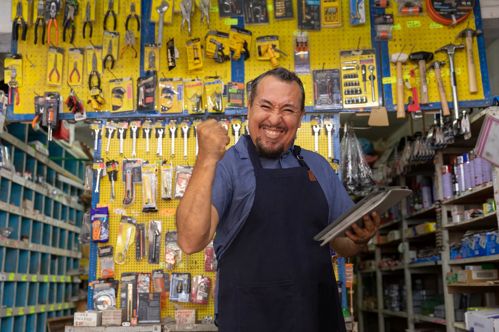 Handsome adult entrepreneur man in apron, with an expression of pride and happiness in her business full of hardware products.
