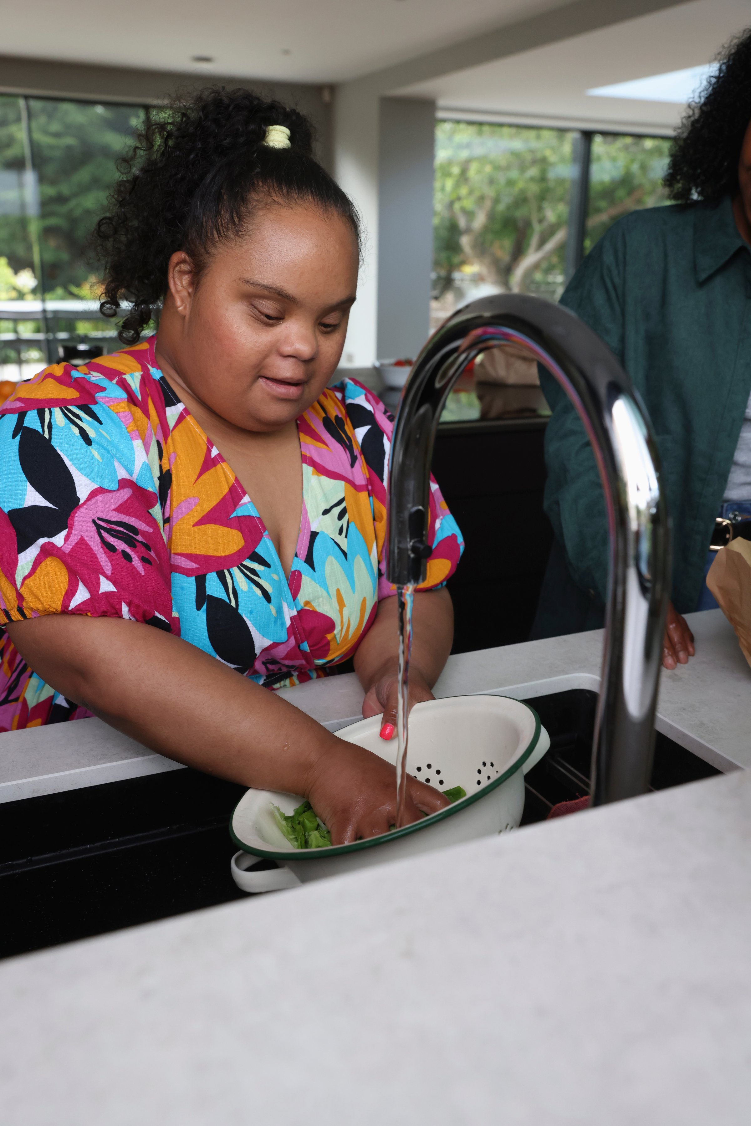 Young woman with Down syndrome washing greens in kitchen sink