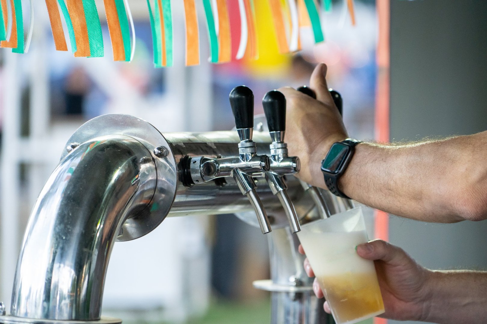 Close-up of a stainless steel beer dispenser with several taps in action. Person pouring a glass of beer. Bartender serving beer. Person filling a glass of alcohol. Man at street fair at a beer stall.