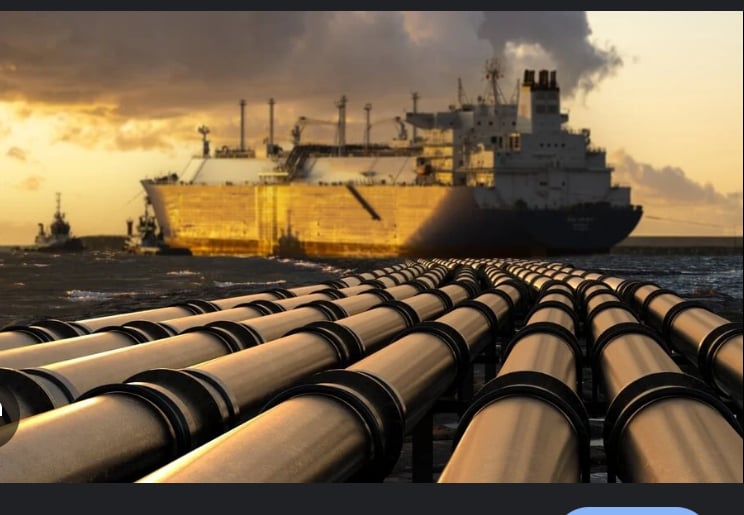 Pipelines leading to a large ship at sea during sunset, with a smaller vessel in the background and dramatic clouds overhead.
