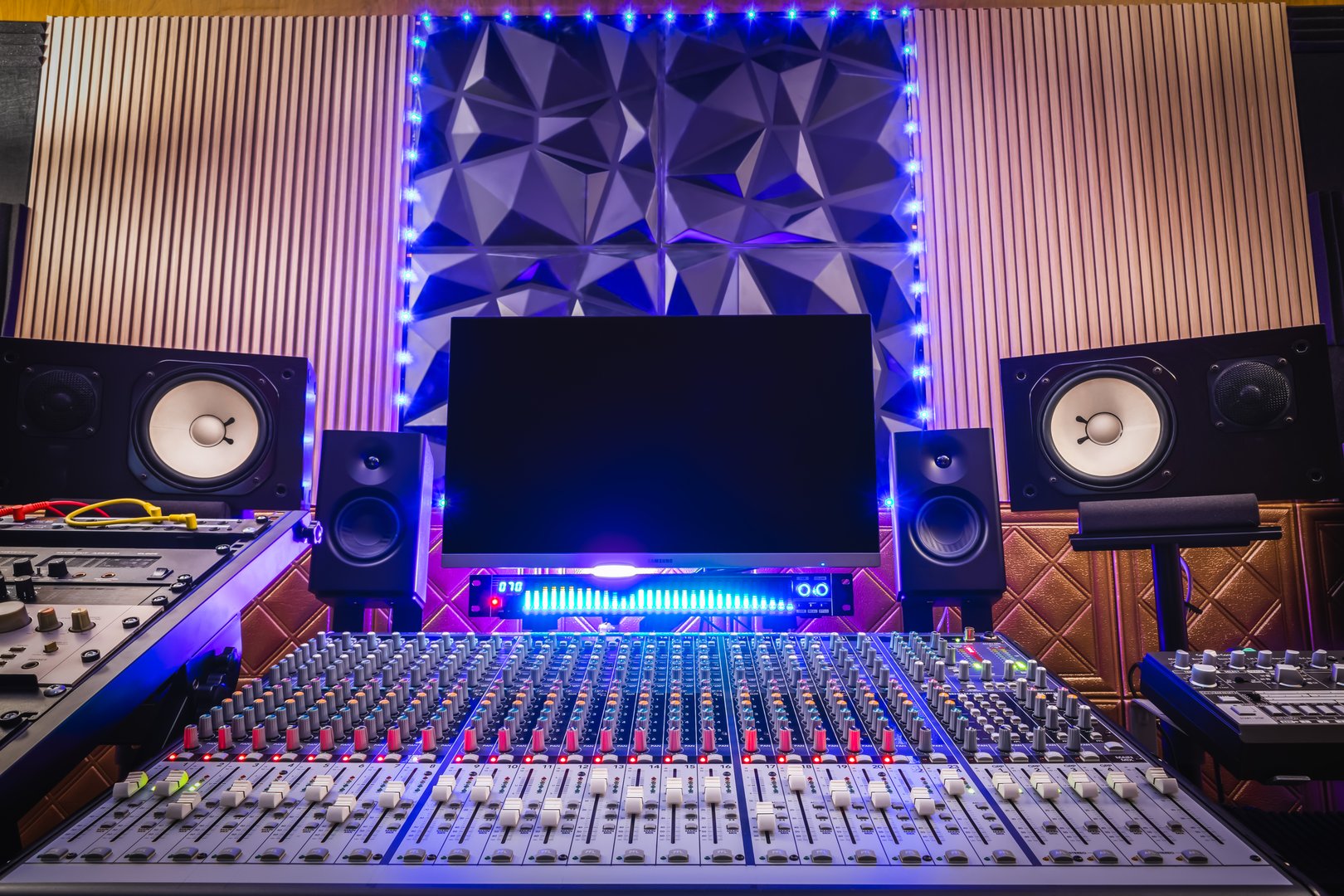 home recording studio. mixing console, studio monitors, desktop computer and professional audio equipment with modern sound diffuser wall design.