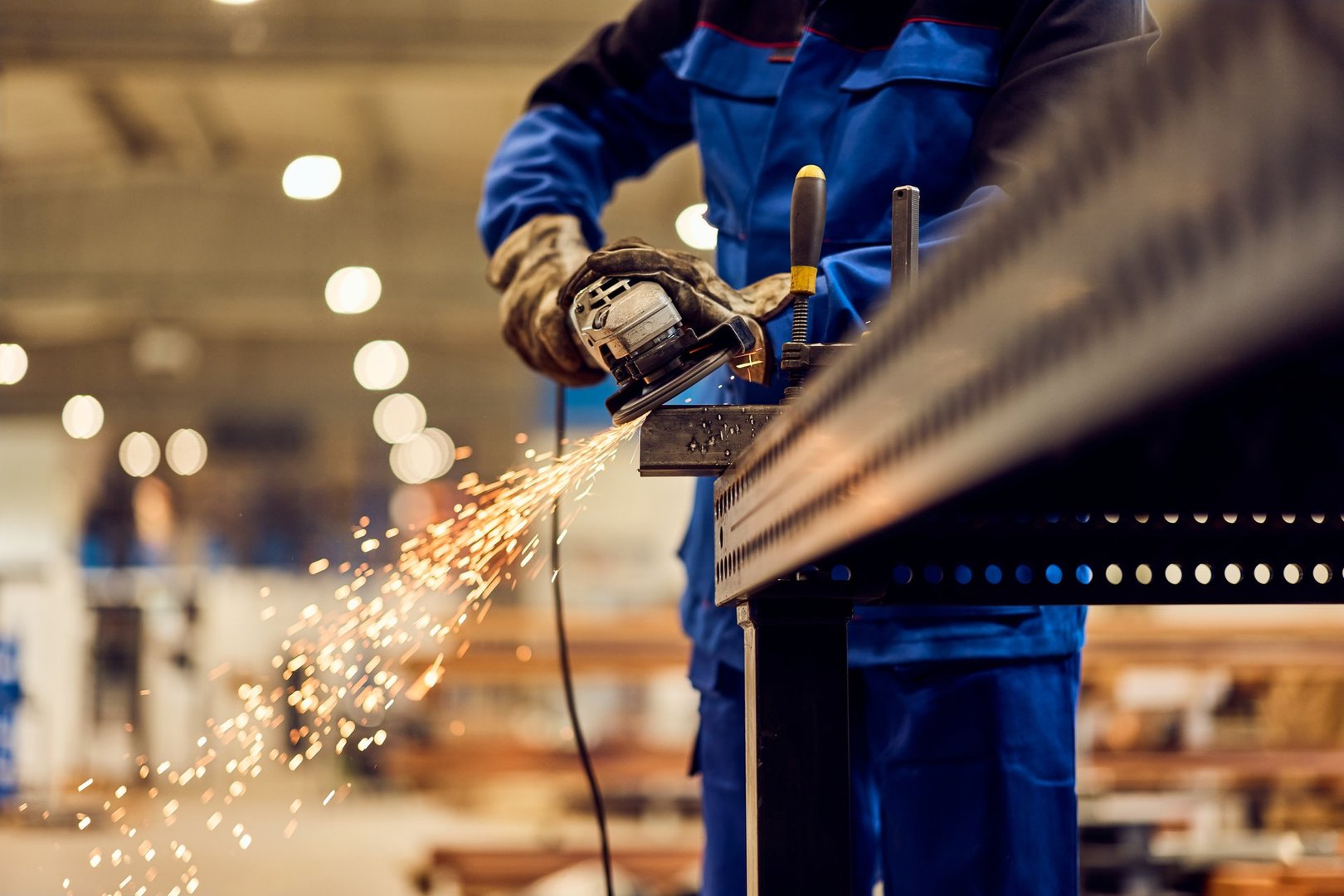 Industrial worker operating power grinder creating sparks in a metalworking environment.
